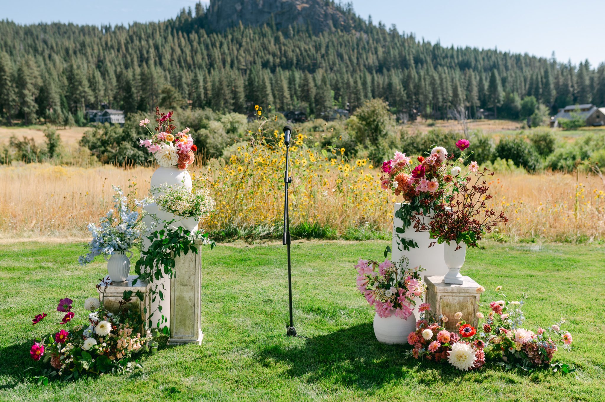 A picturesque outdoor ceremony site framed by lush florals in white, blush, and deep red hues, set against the breathtaking mountain and forest landscape.
