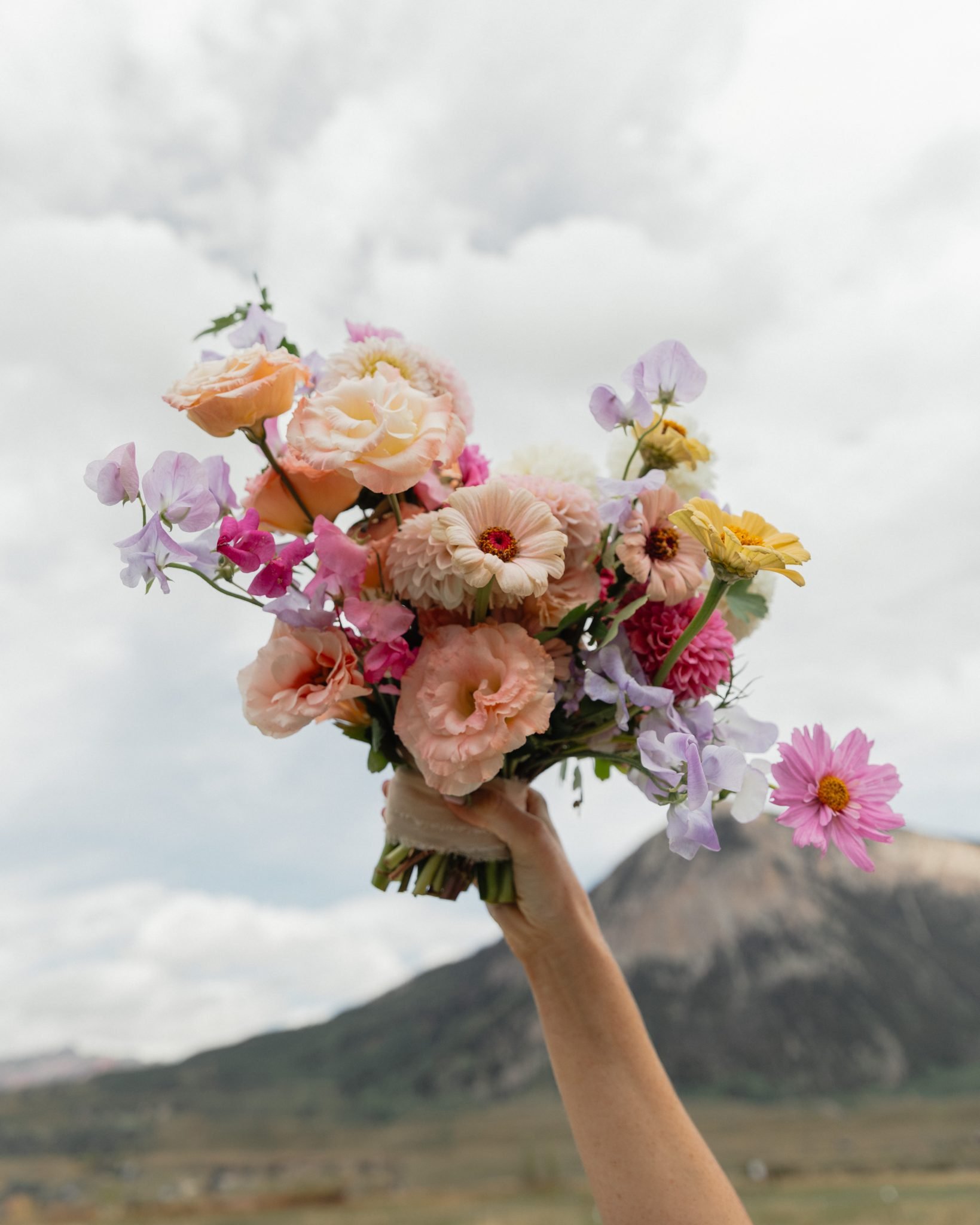 Vibrant bridal bouquet with pastel flowers held high at a pink and yellow Crested Butte wedding rocky mountain bride