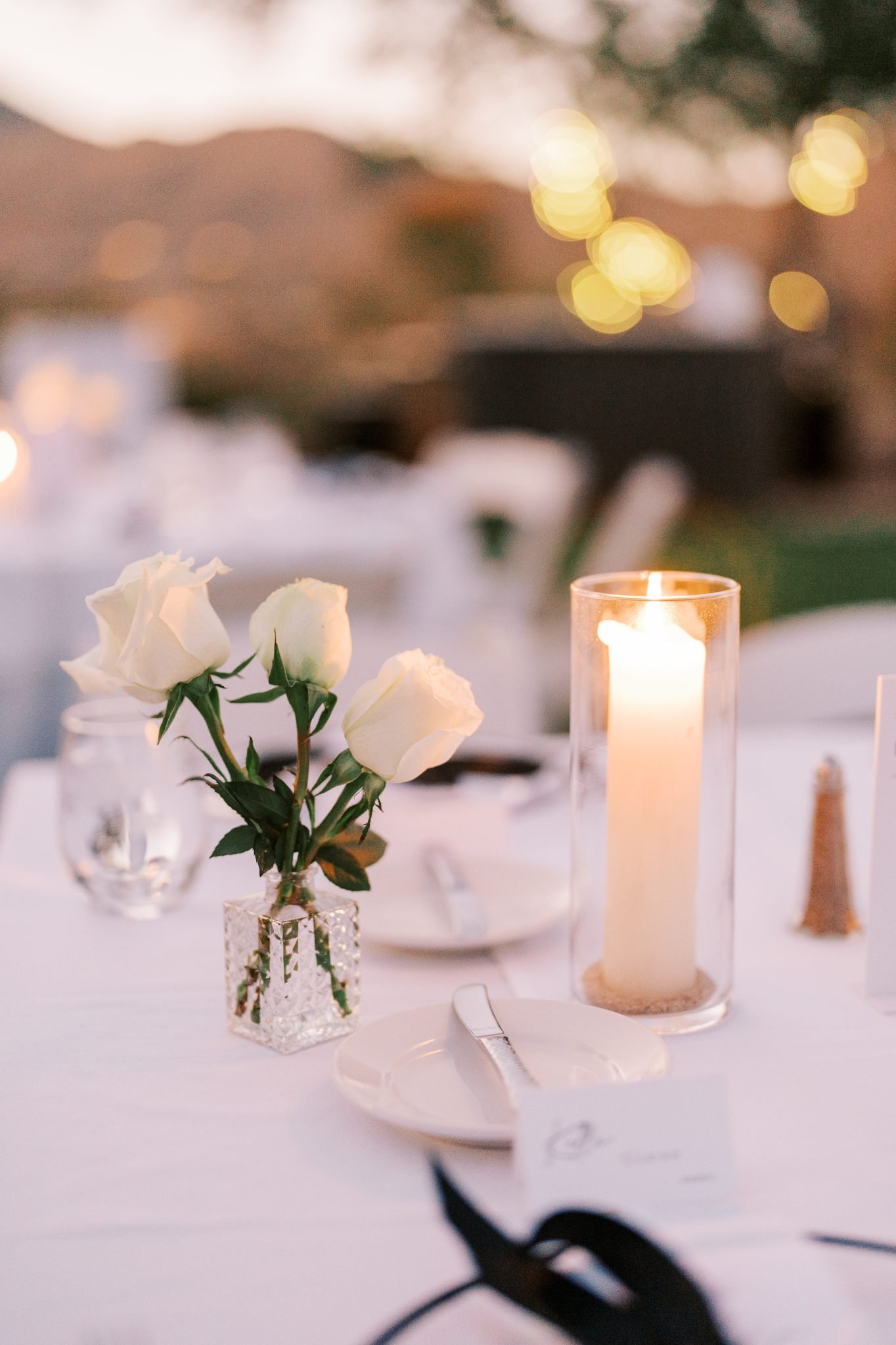 Table centerpiece featuring white roses and a tall candle in a glass holder at Adero Scottsdale Resort white and black wedding.