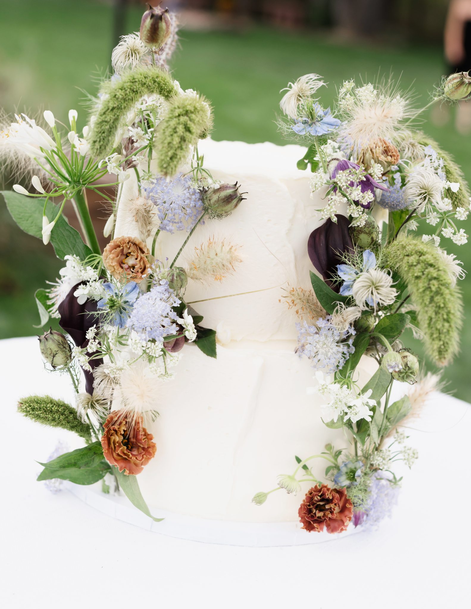 Two-tiered buttercream wedding cake decorated with fresh wildflowers and greenery for a Boulder flower farm wedding.