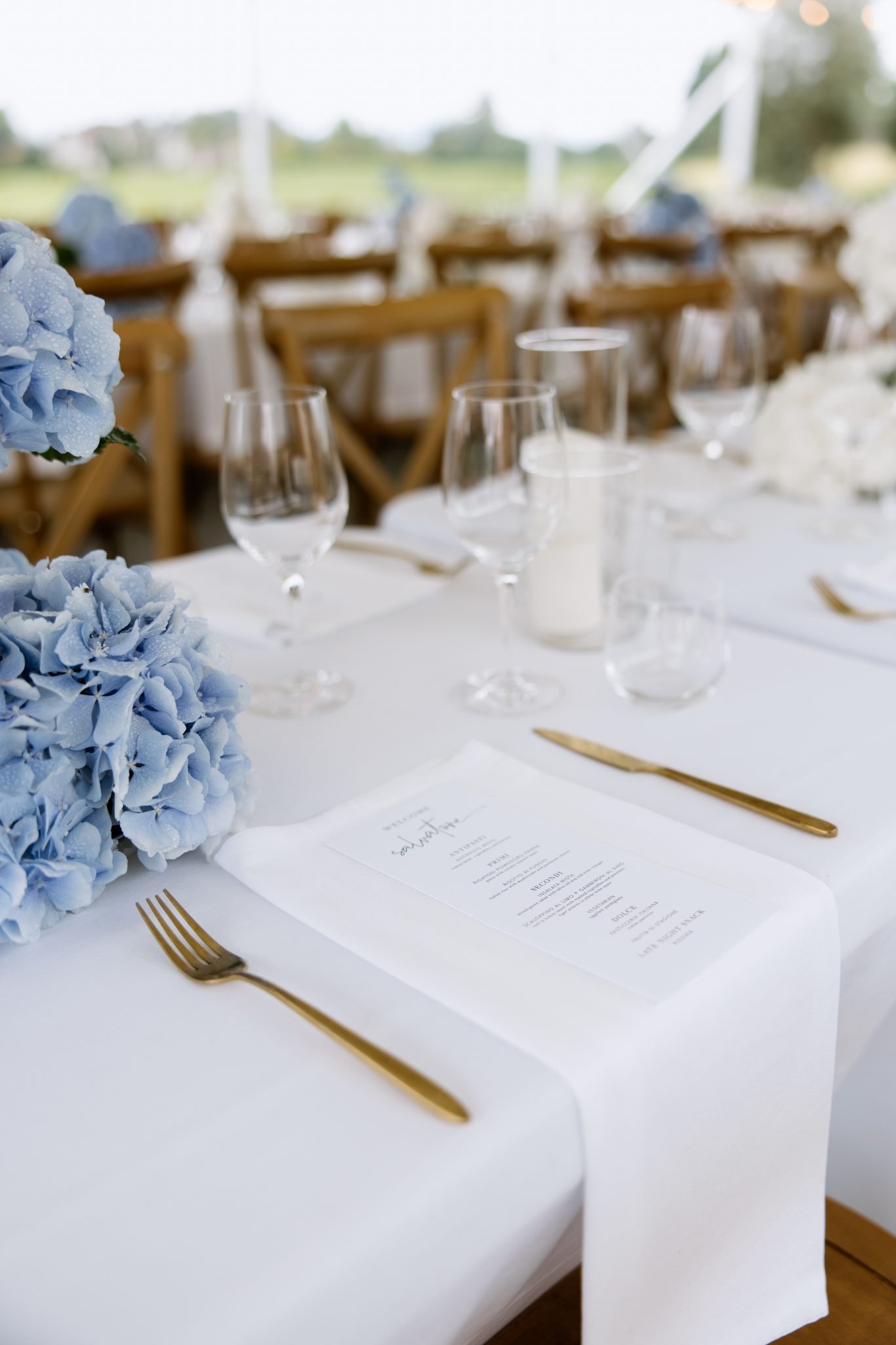 Refined summer tablescape with blue hydrangeas, white linens, and gold flatware at a Cannon Estate Vineyard summer elevated wedding.