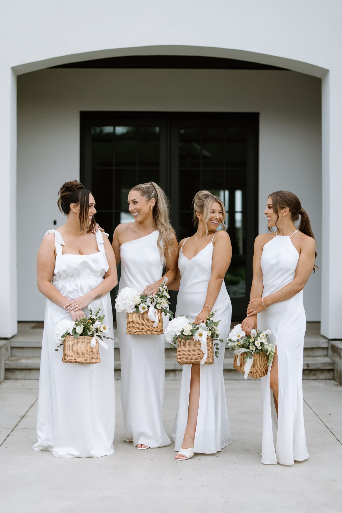 Bridesmaids in white dresses holding wicker basket bouquets at the Cannon Estate Vineyard summer elevated wedding.