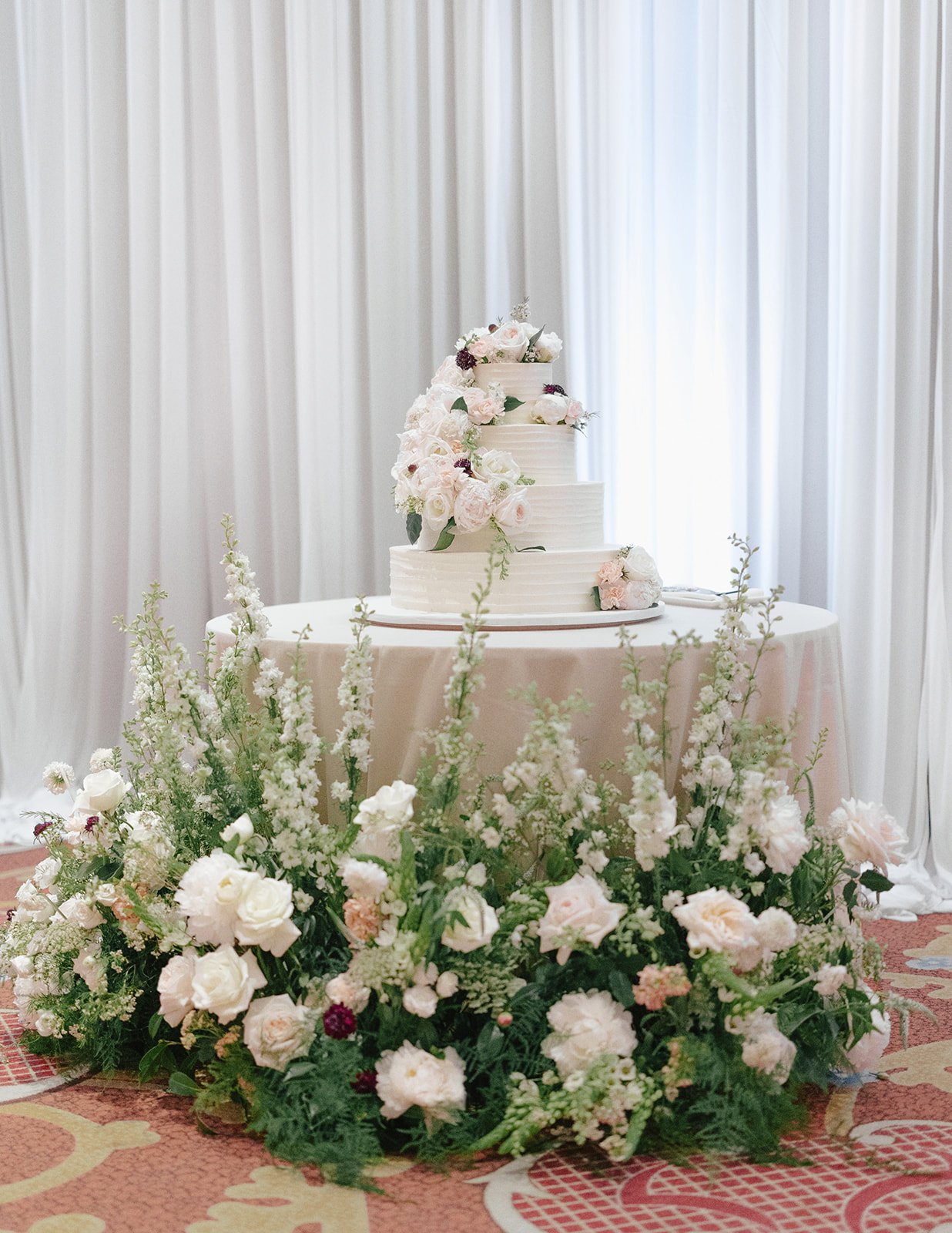 Three-tiered white wedding cake with cascading blush flowers and floral base décor at an Elegant Wynn Las Vegas wedding.