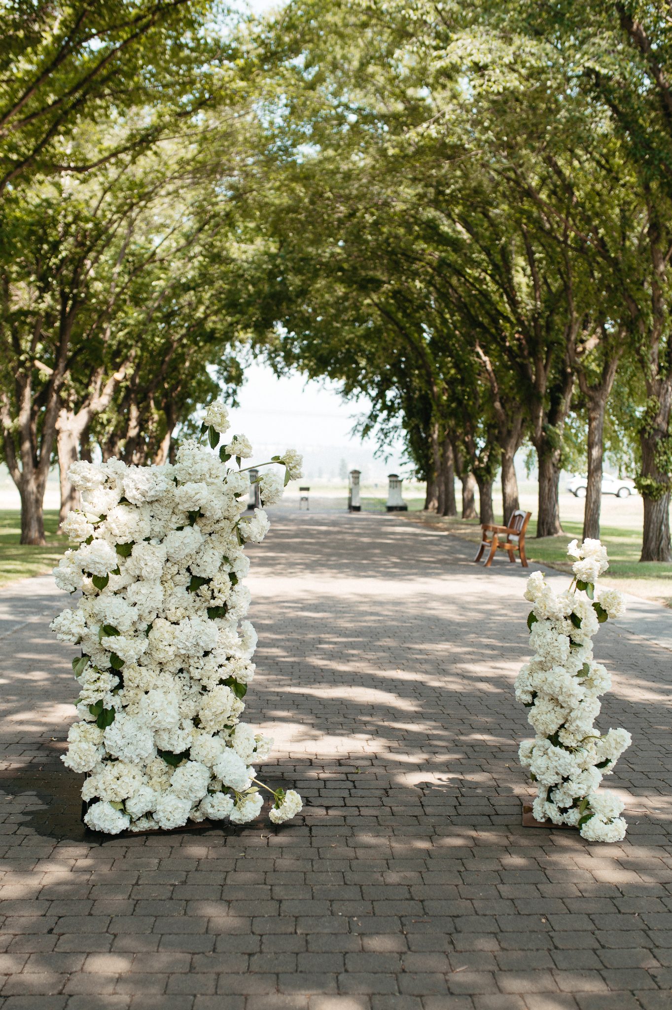 Romantic outdoor ceremony setup with white floral pillars under a tree-lined path at St. Eugene Golf Resort & Casino British Columbia wedding