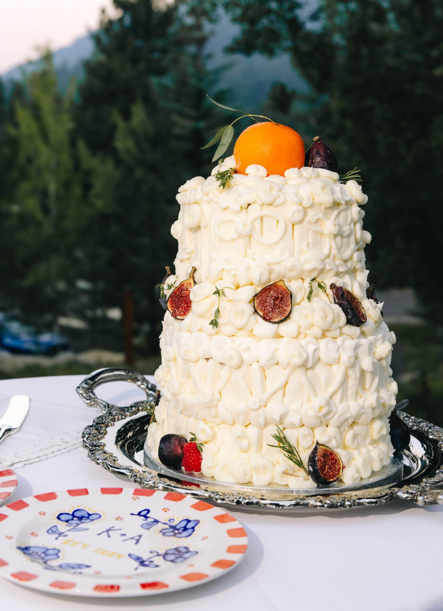 A textured, buttercream-covered tiered wedding cake topped with citrus and figs sits on a silver tray during a Tamarack Resort summer wedding reception.