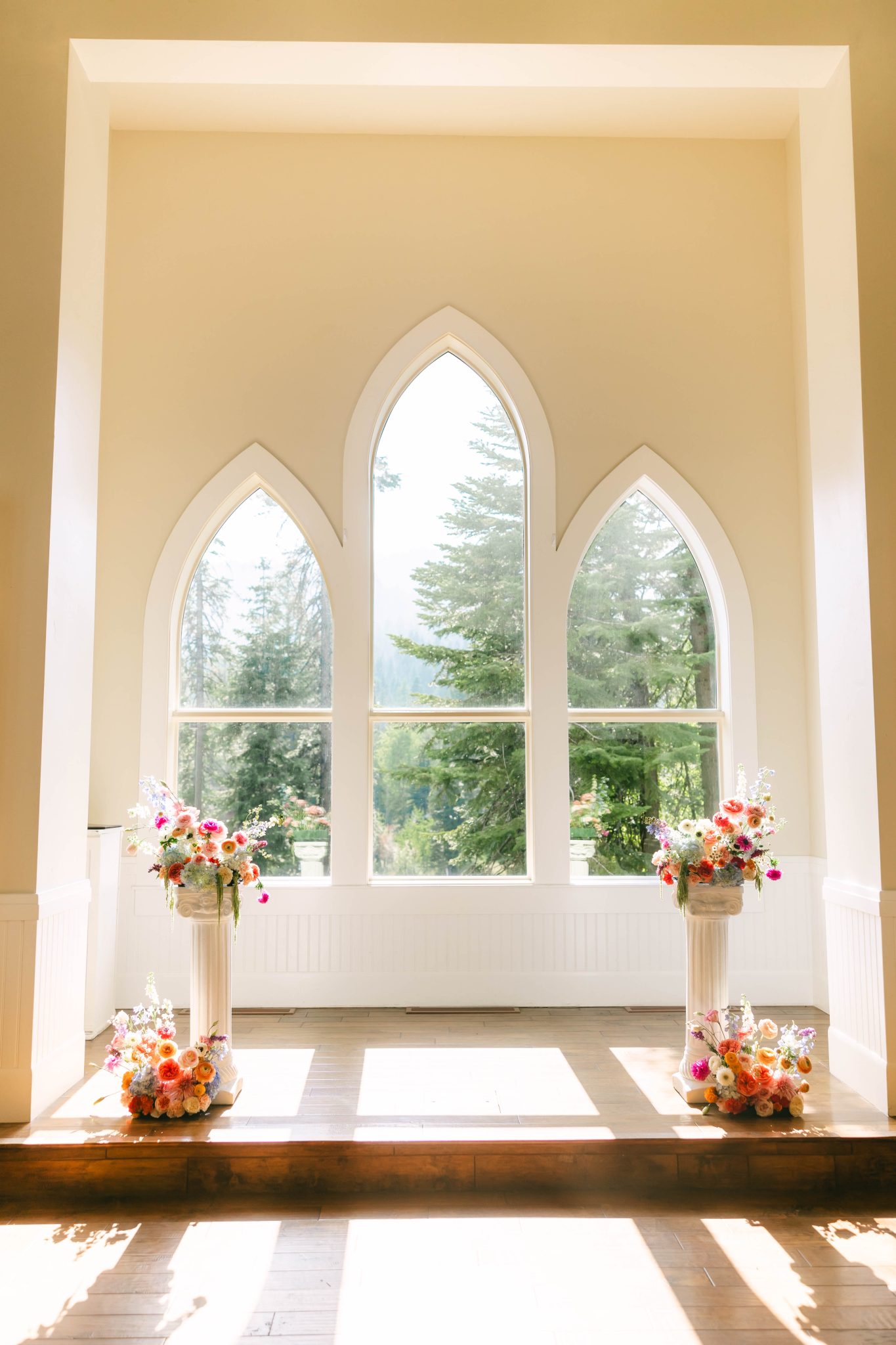Sunlight floods a chapel with arched windows and colorful floral columns for a Tamarack Resort summer wedding ceremony.