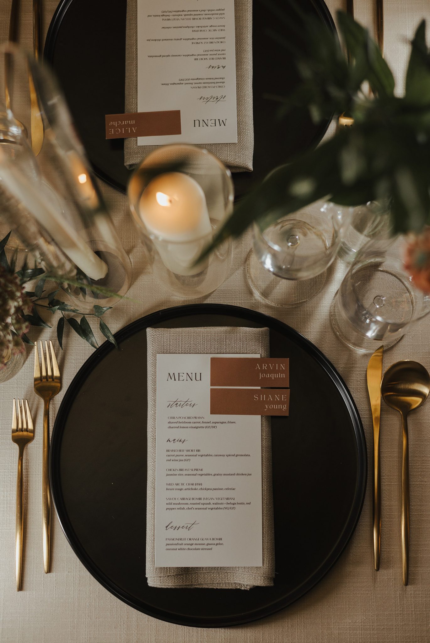 Elegant table setting with black plates, gold flatware, and custom menus at The Permanent summer wedding in British Columbia rocky mountain bride reception dinner.
