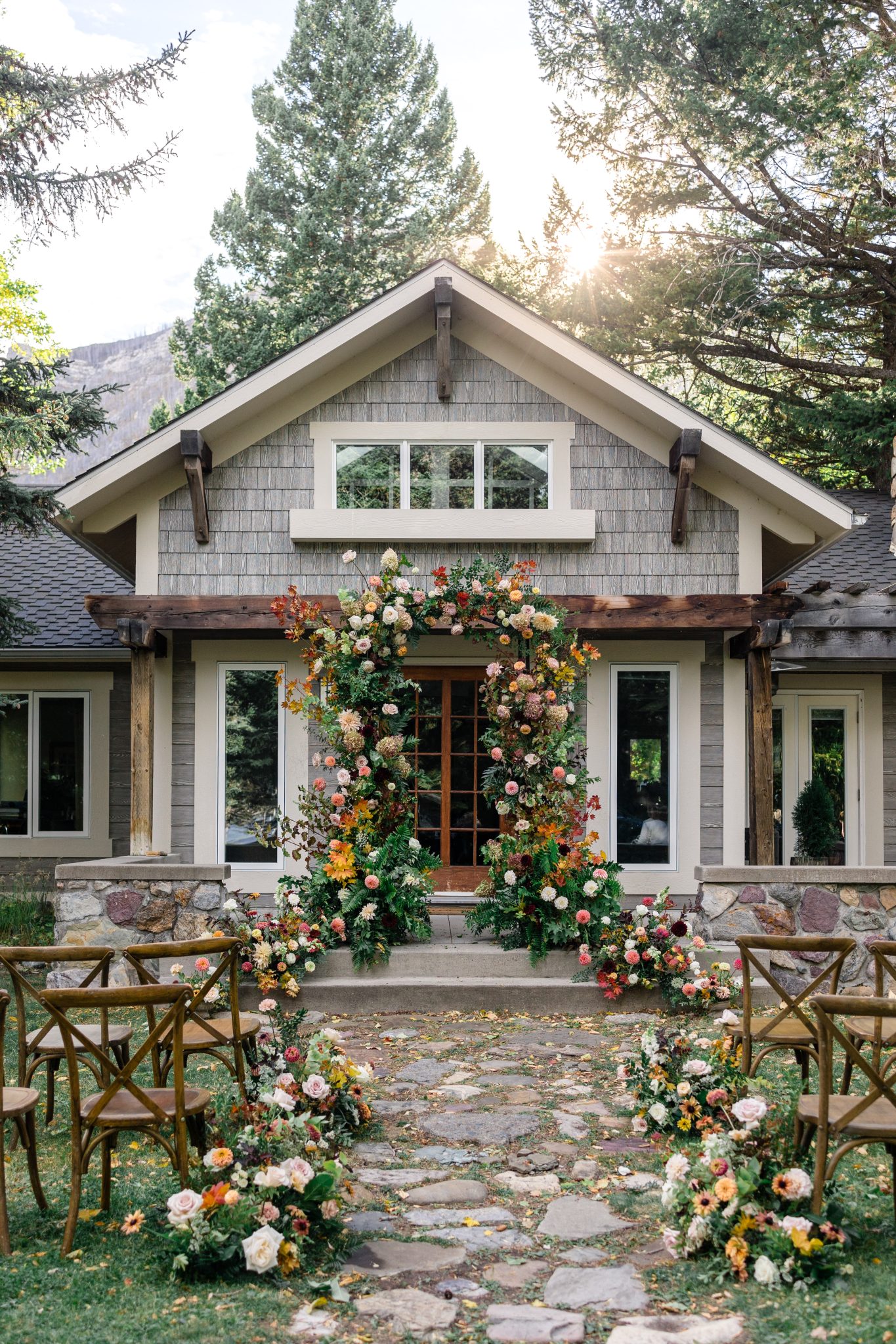 Charming ceremony setup with a lush floral arch in front of a cottage for a romantic Waterton Lakes National Park styled shoot.