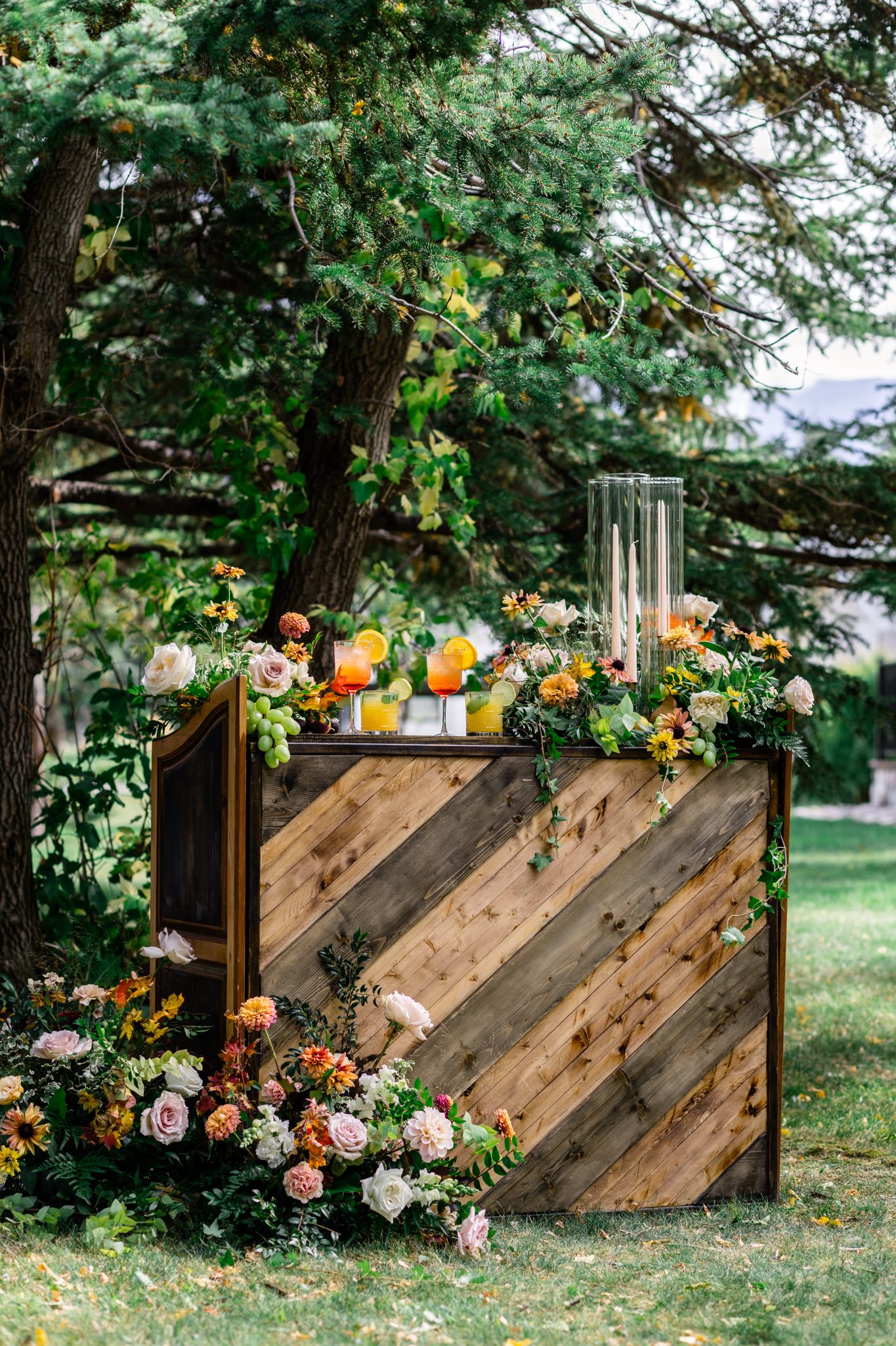 Rustic outdoor wedding bar decorated with fresh flowers, grapes, and colorful cocktails during a Waterton Lakes National Park styled shoot.