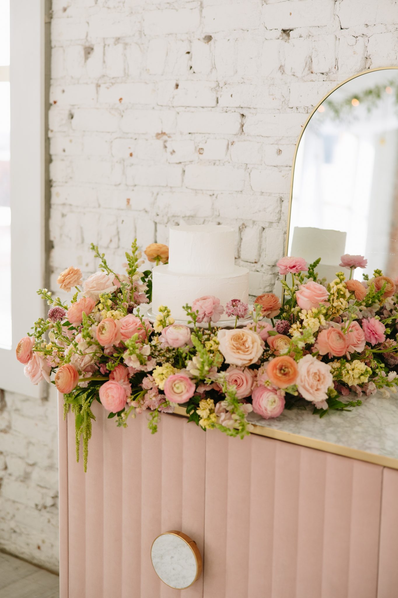 Floral-decorated cake table with vintage pink sideboard and mirror setup captured for indoor utah wedding inspiration rocky mountain bride.