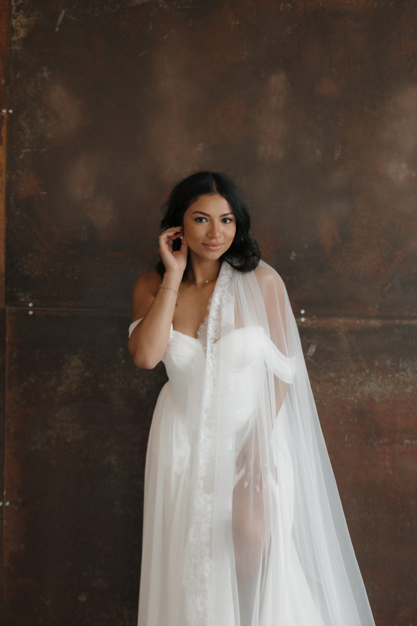 Stunning bride in a flowing veil poses against a moody textured wall, styled for indoor utah wedding inspiration rocky mountain bride.