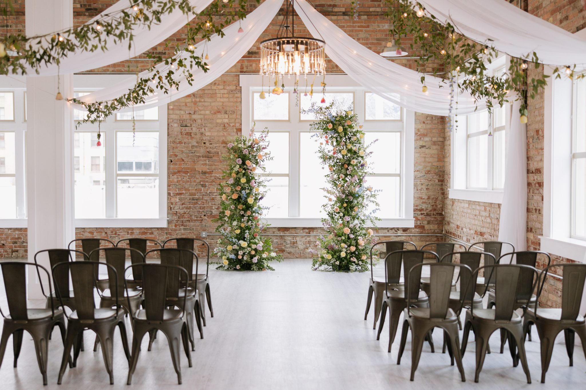 Industrial-chic ceremony space featuring floral pillars and draped fabric details designed for indoor utah wedding inspiration rocky mountain bride.