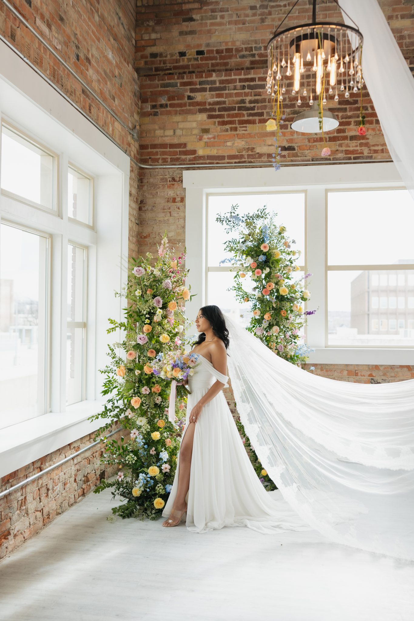 Elegant bride poses in front of lush floral pillars in a bright loft venue for indoor utah wedding inspiration rocky mountain bride.