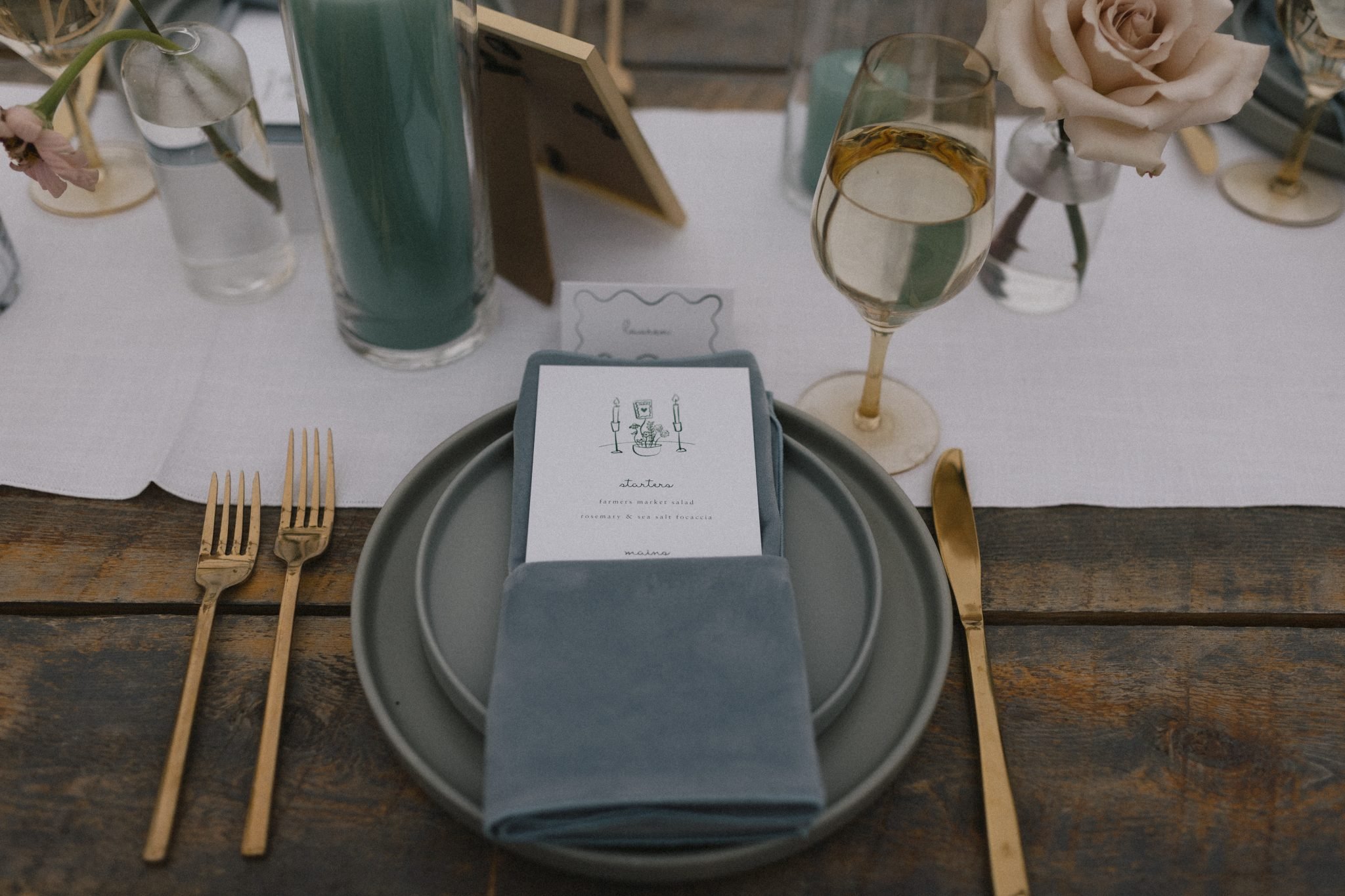 Elegant place setting featuring dusty blue napkins, gold flatware, and minimal floral details for Blackstone Rivers Ranch colorado wedding rocky mountain bride.