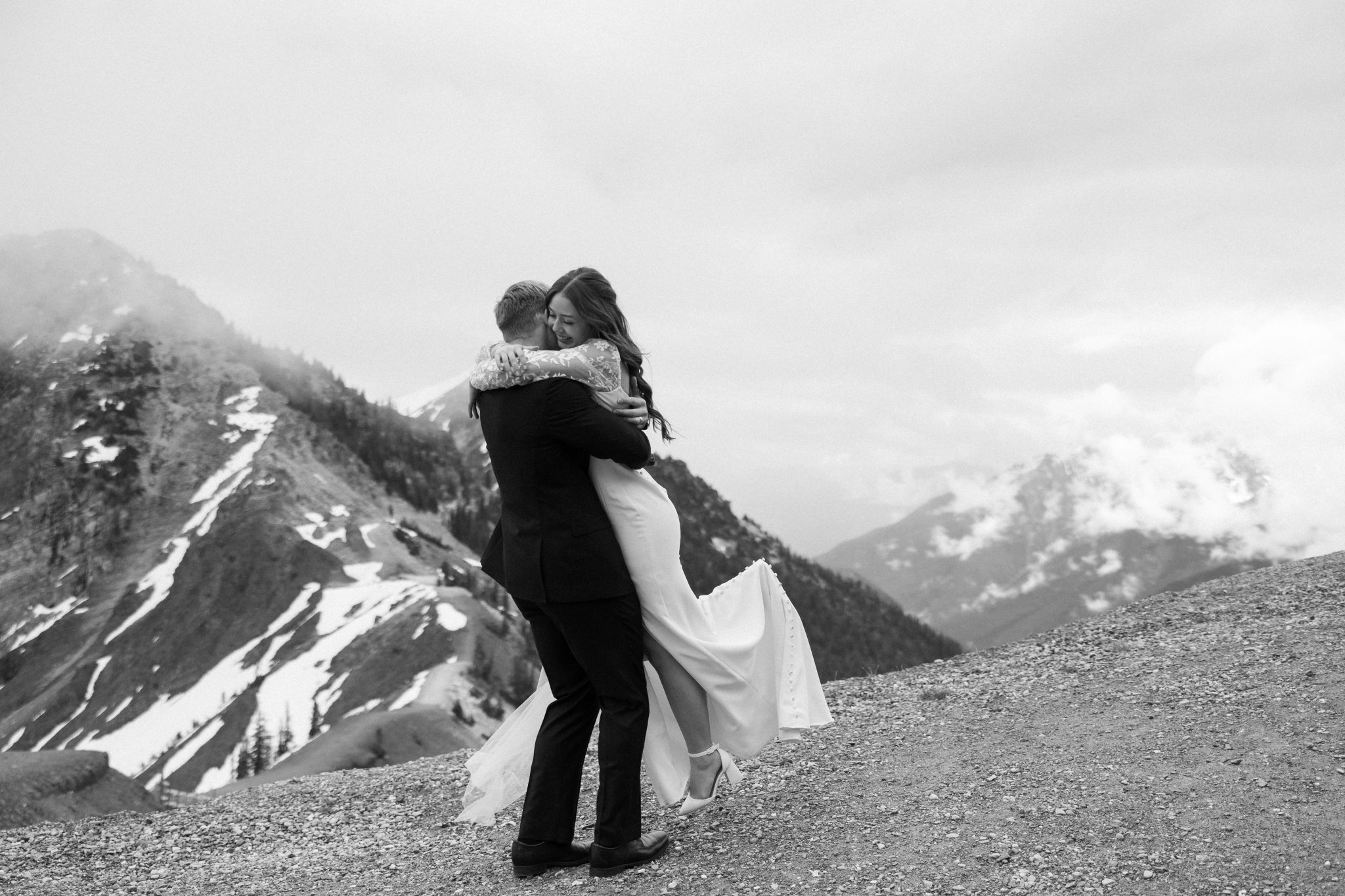 Couple embraces on a foggy mountaintop, celebrating their Golden british columbia spring wedding rocky mountain bride with dramatic alpine views.