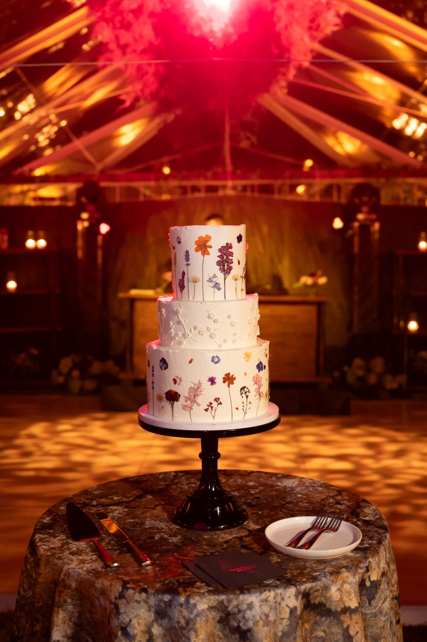 Three-tiered cake with pressed floral designs displayed under moody lighting at a Heritage Ranch fall wedding rocky mountain bride.