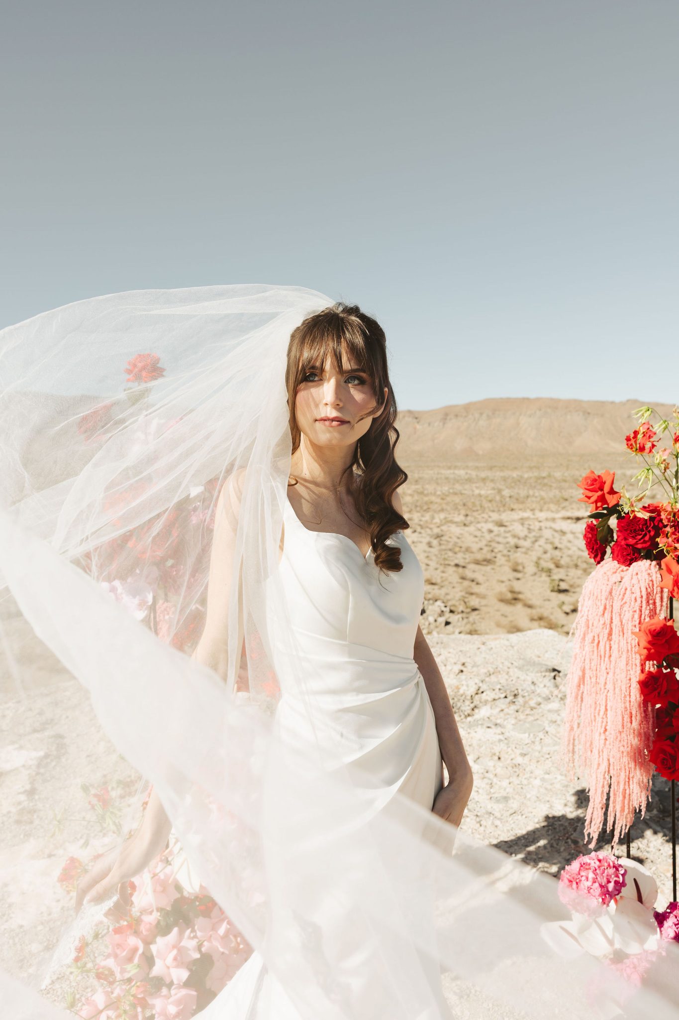 Bride poses with veil flowing and bold red, pink, and coral bouquet at the Riann Hassell styled shoot las vegas nevada rocky mountain bride in a high-desert setting.