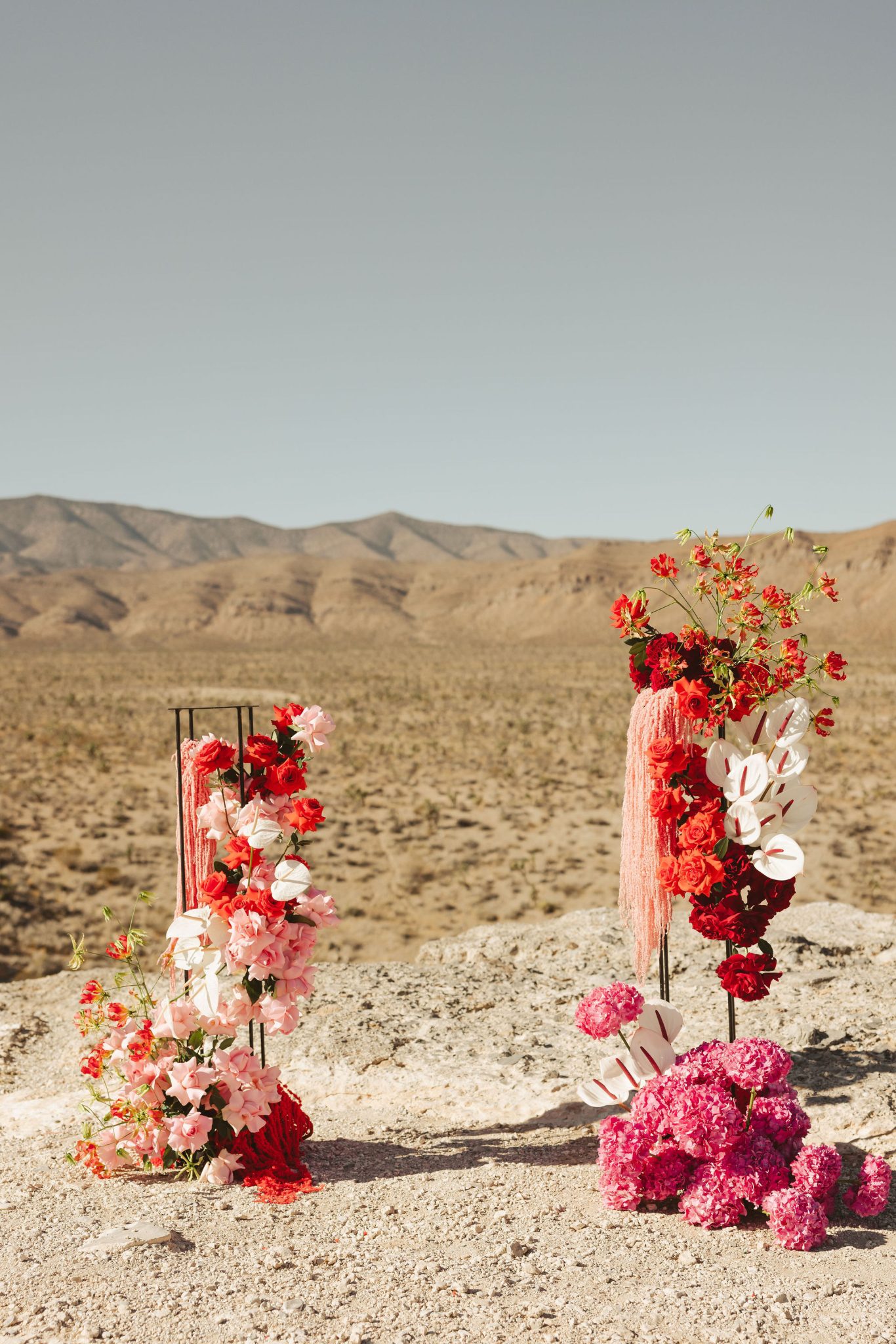 Abstract floral pillars with red, blush, and coral blooms at a desert ceremony site for the Riann Hassell styled shoot las vegas nevada rocky mountain bride.