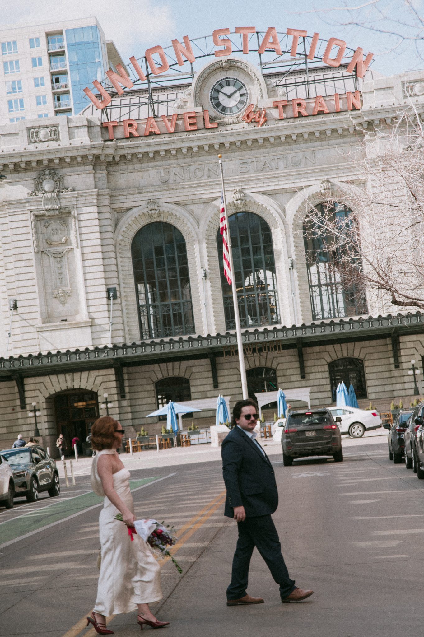 A couple crosses the street outside Union Station in Denver, bouquet in hand, during their Salt Photography engagement rocky mountain bride session.