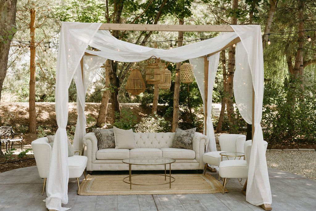 Neutral-toned lounge seating area with hanging rattan lanterns and floral arrangements at Willow Creek Wedding and Events Idaho rocky mountain bride venue.