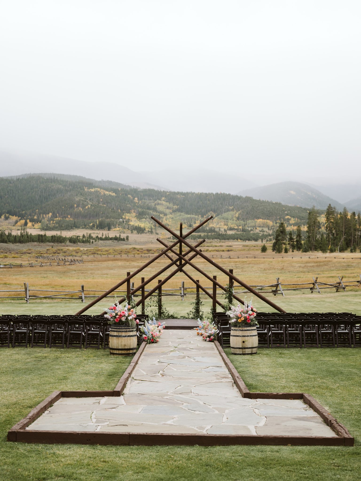 Outdoor ceremony site with wooden altar structure, floral barrels, and mountain landscape for a colorado wedding rocky mountain bride editorial.