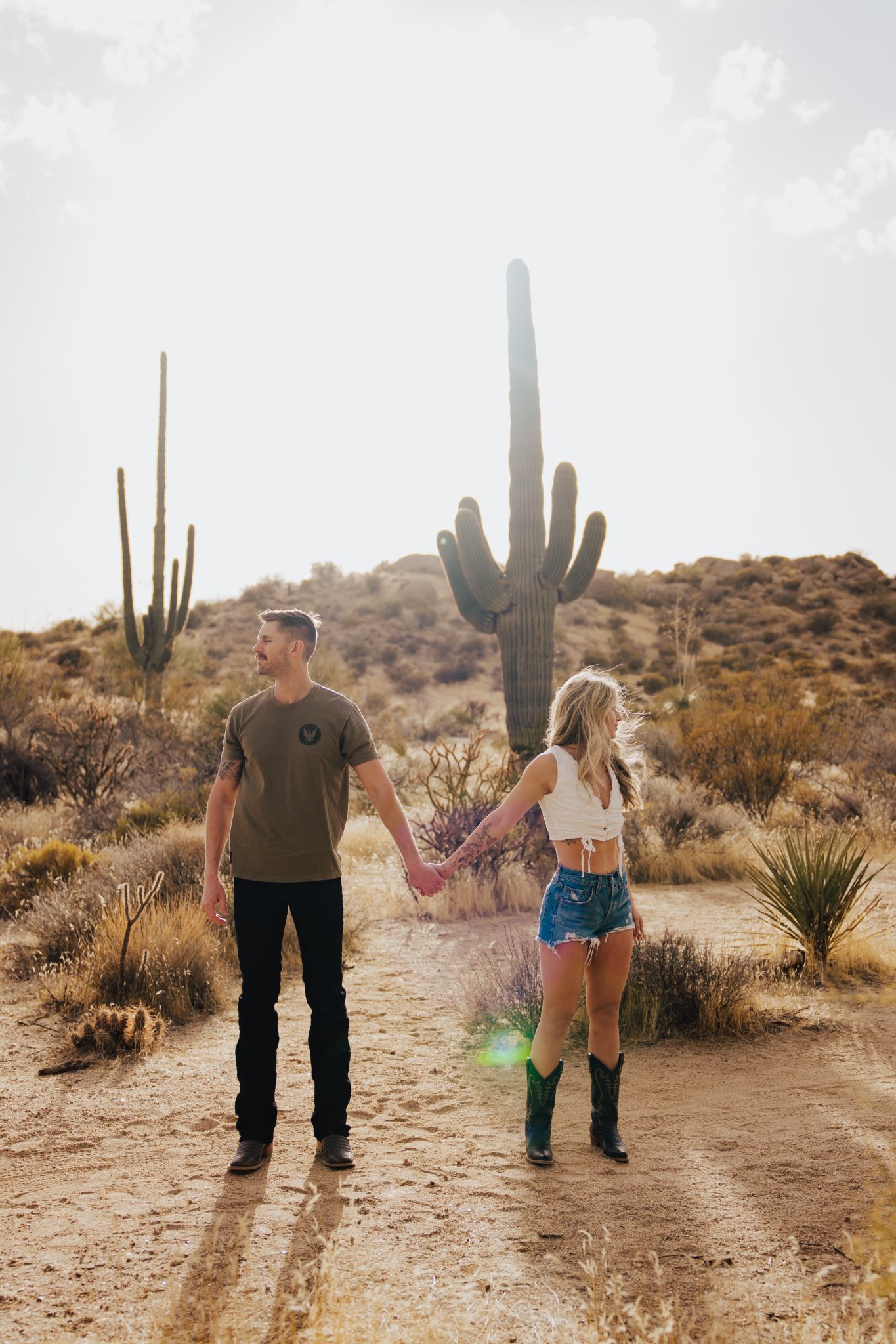 Couple holding hands in front of a saguaro cactus at sunset during an Arizona desert engagement session rocky mountain bride feature.