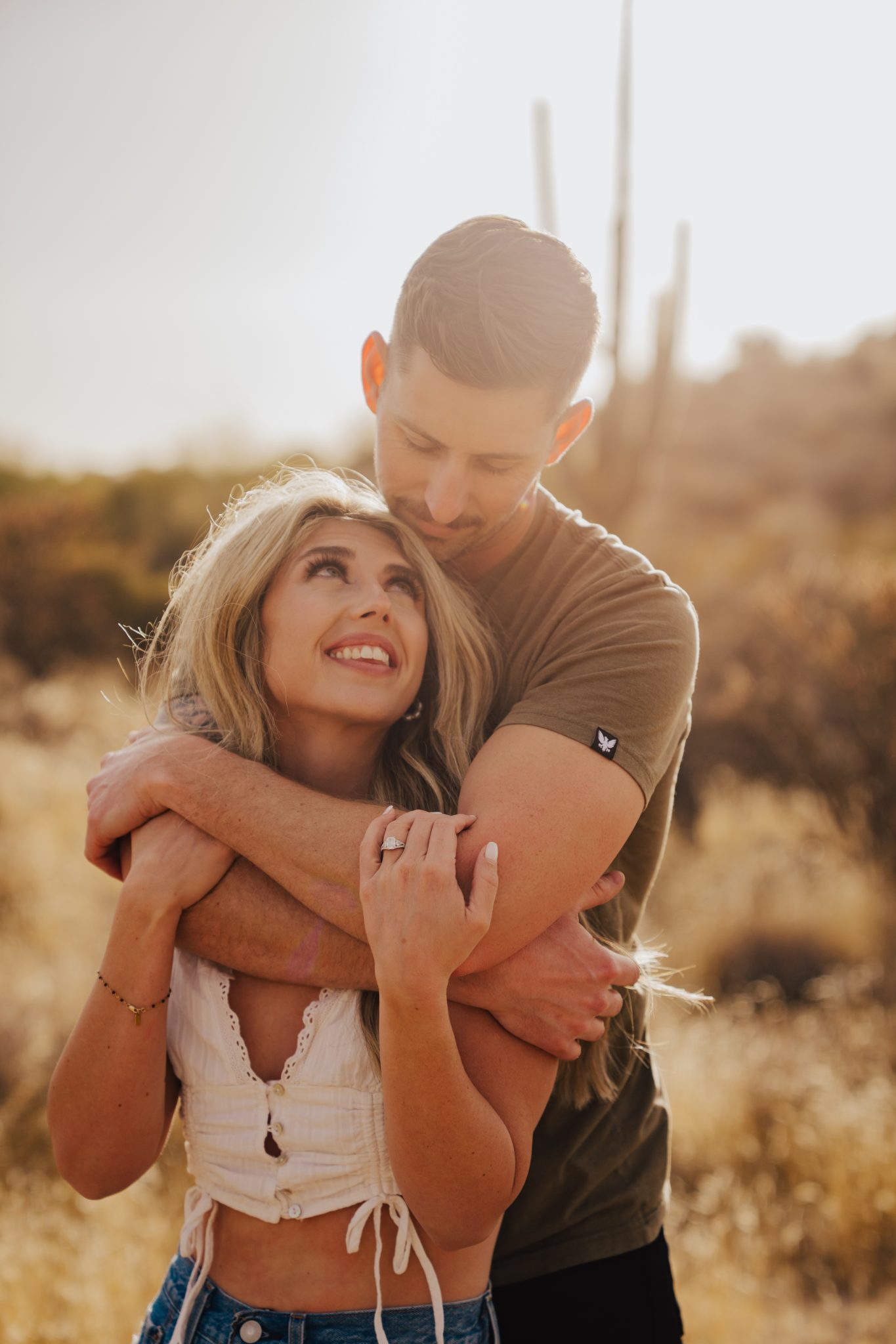 Close-up of couple embracing in golden desert light during their Arizona desert engagement session rocky mountain bride story.