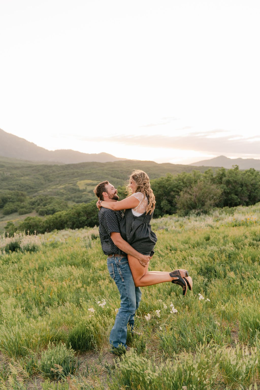 A joyful lift-and-spin moment between a couple in a wildflower field with mountain views, photographed by Christensen Edits Photography Utah engagement session rocky mountain bride.