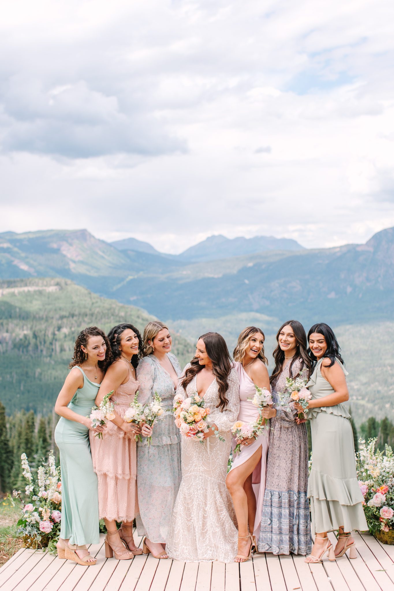 The bride surrounded by bridesmaids in pastel dresses at Purgatory Resort winter wedding rocky mountain bride, with sweeping mountain views behind them.