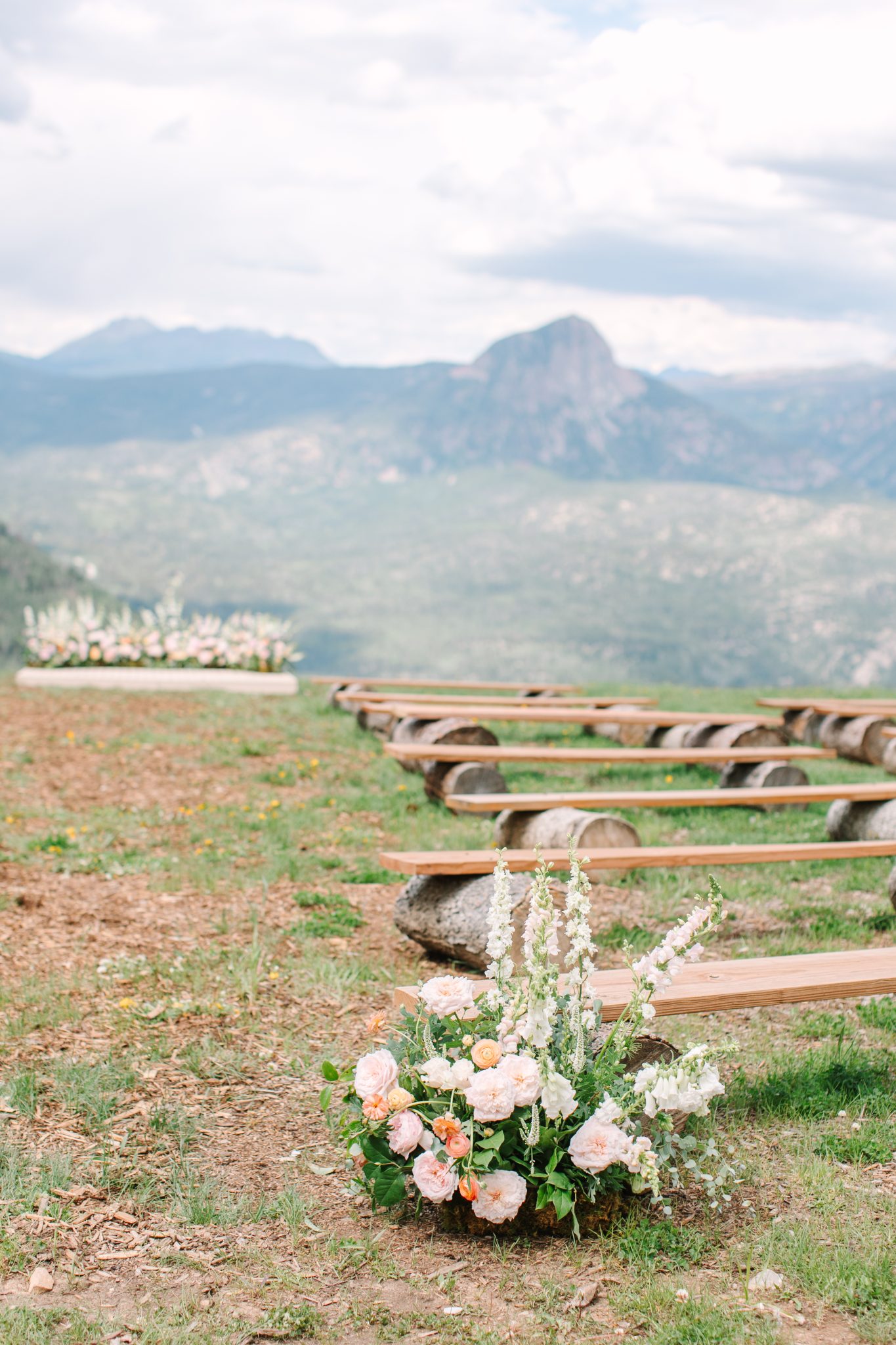 Rustic ceremony seating with log benches and fresh florals set for a Purgatory Resort winter wedding rocky mountain bride against scenic mountain peaks.