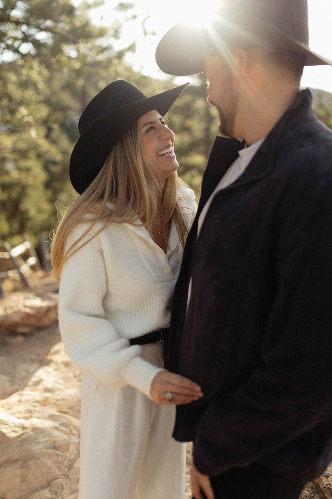 A joyful couple in wide-brim hats laugh together at sunset during their S Lynne Photography Boulder Colorado engagement session rocky mountain bride.