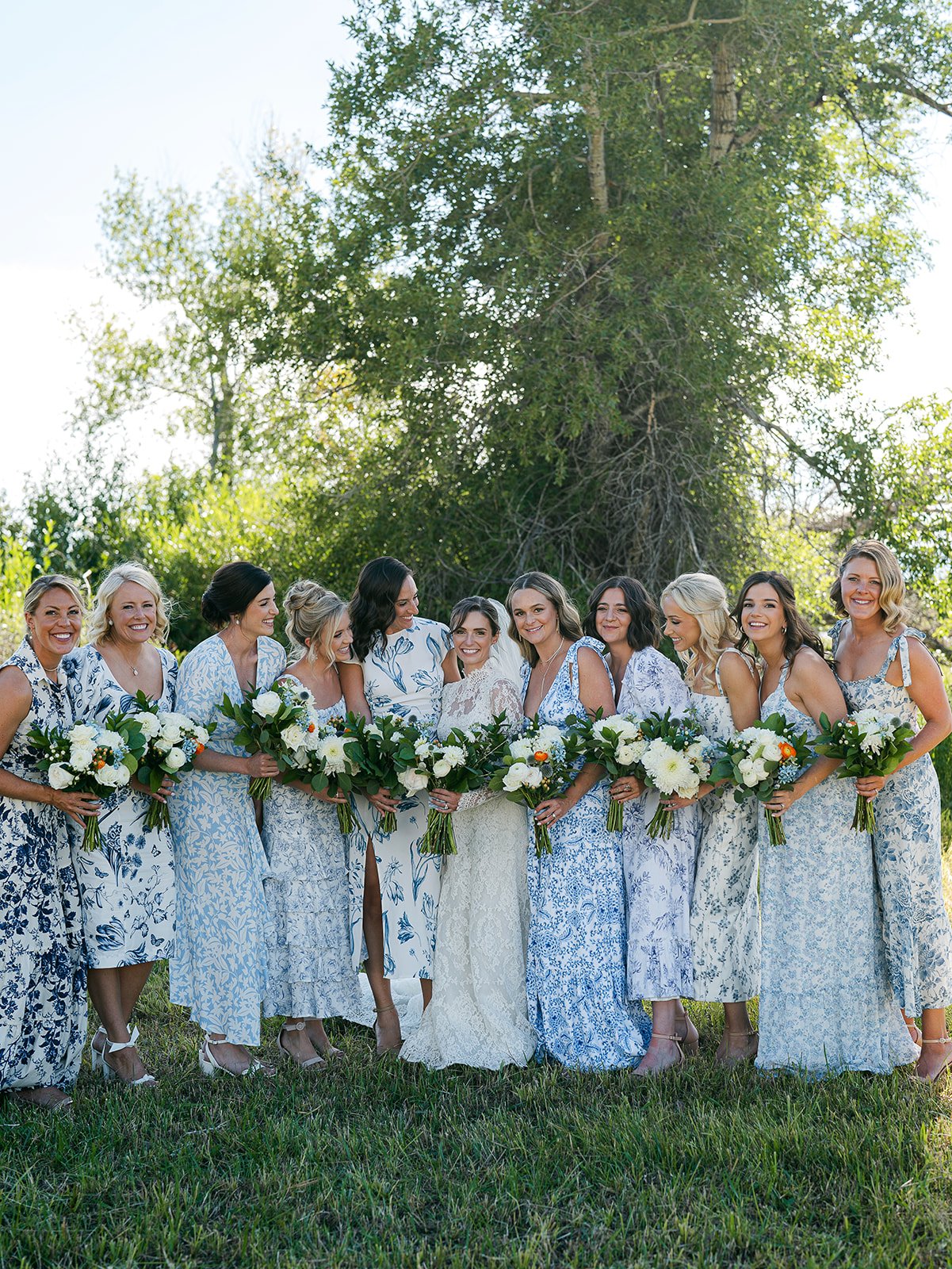 Bride surrounded by bridesmaids in coordinated blue and white floral dresses holding bouquets at a Saratoga private residence wedding Wyoming Rocky Mountain Bride.
