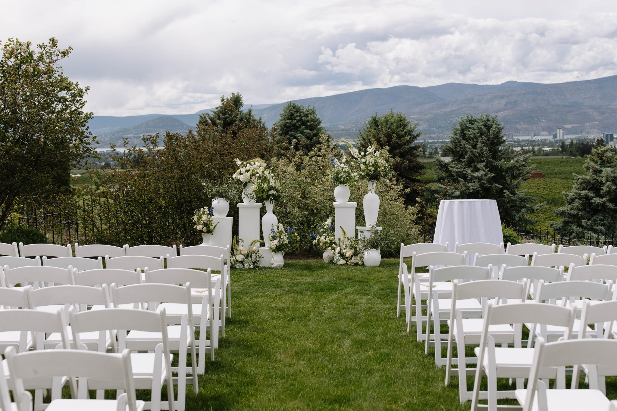 A romantic outdoor ceremony at The Vibrant Vine summer wedding rocky mountain bride featuring white chairs, floral columns, and sweeping vineyard and mountain views.