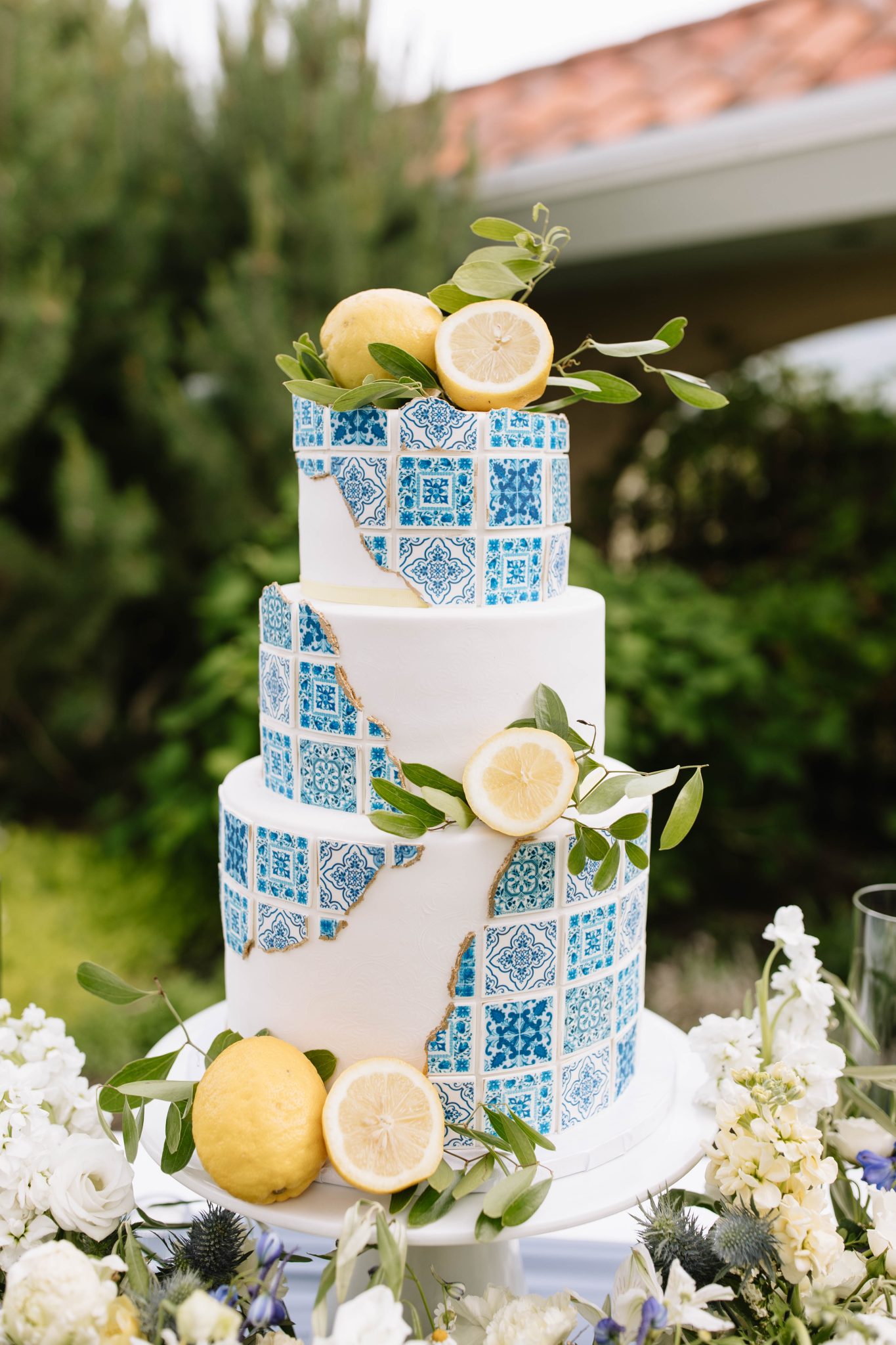 Mediterranean-inspired wedding cake decorated with lemons and blue tile patterns surrounded by florals at The Vibrant Vine summer wedding rocky mountain bride.