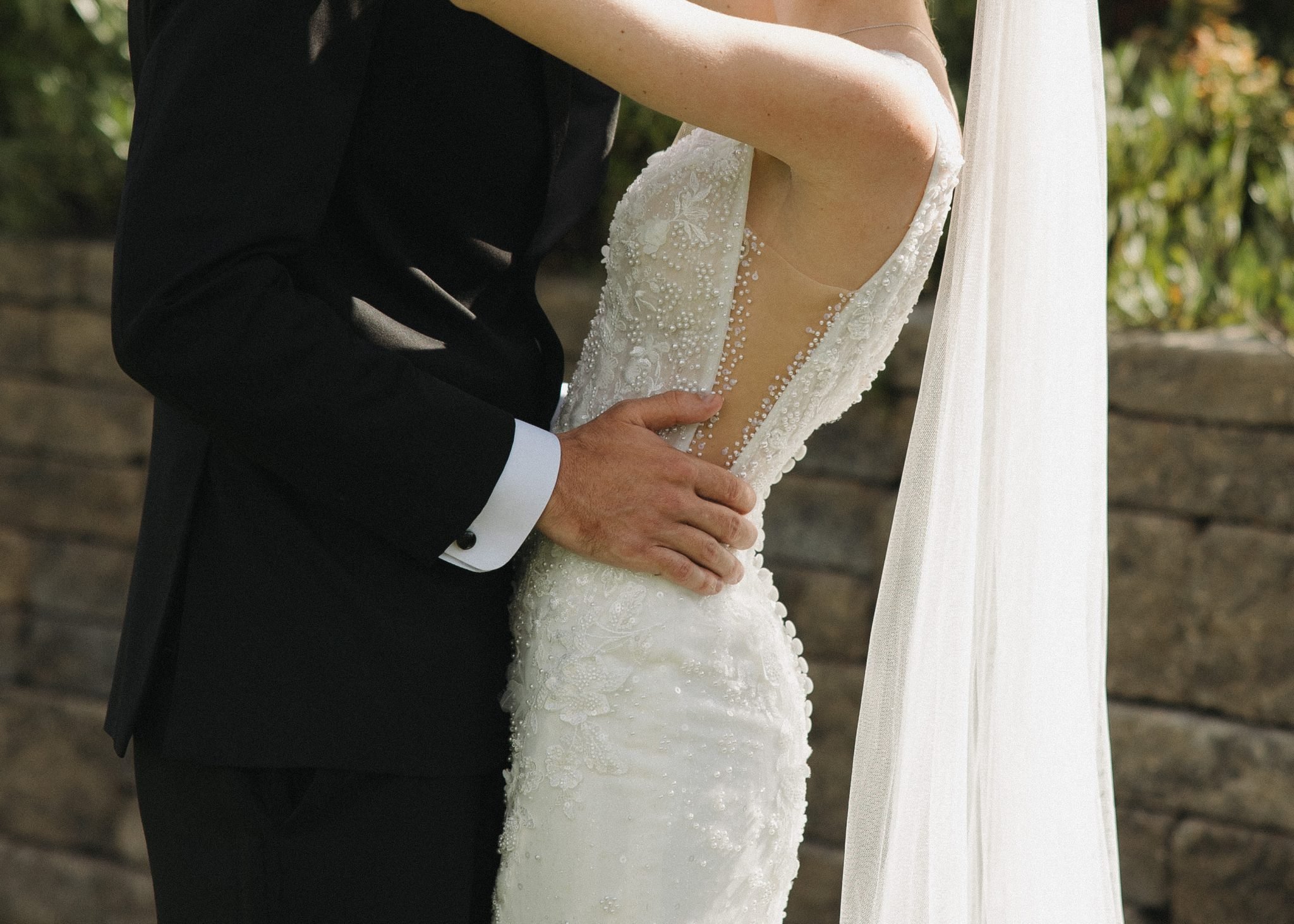 Bride and groom embrace in a lush garden with a stone wall backdrop during their colorado spring wedding bonnie blues event venue rocky mountain bride celebration.