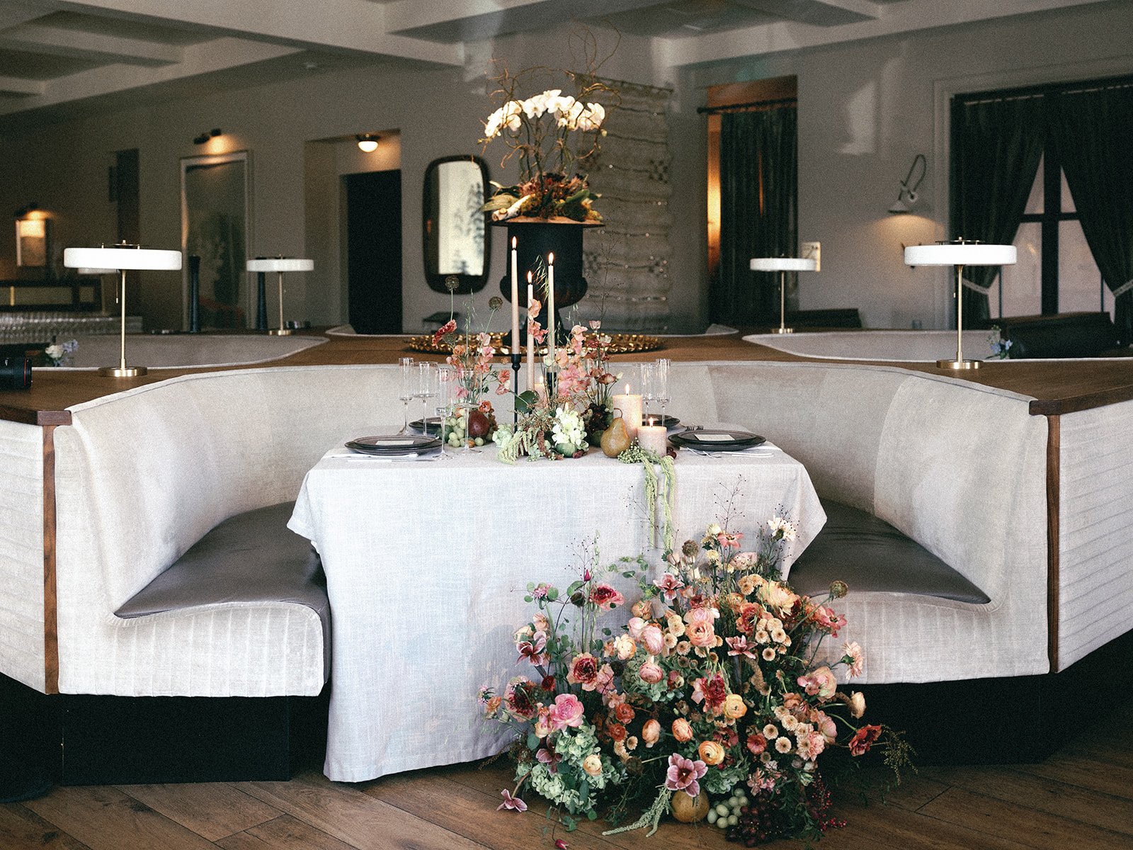 Romantic booth dining scene with a modern tablescape and overflowing floral arrangements for an editorial bride modern tablescape chic wedding the lively downtown boise idaho floral heavy intimate reception dinner pink film elopement.