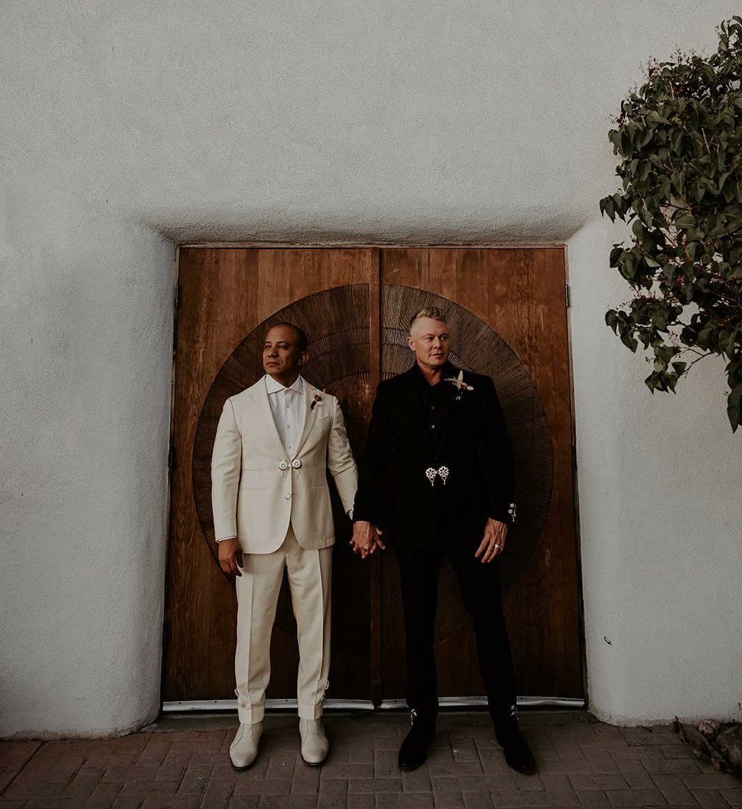 Intimate photo of grooms holding hands in front of large wooden doors at The Stakeout with Suroeste Studios summer wedding rocky mountain bride.