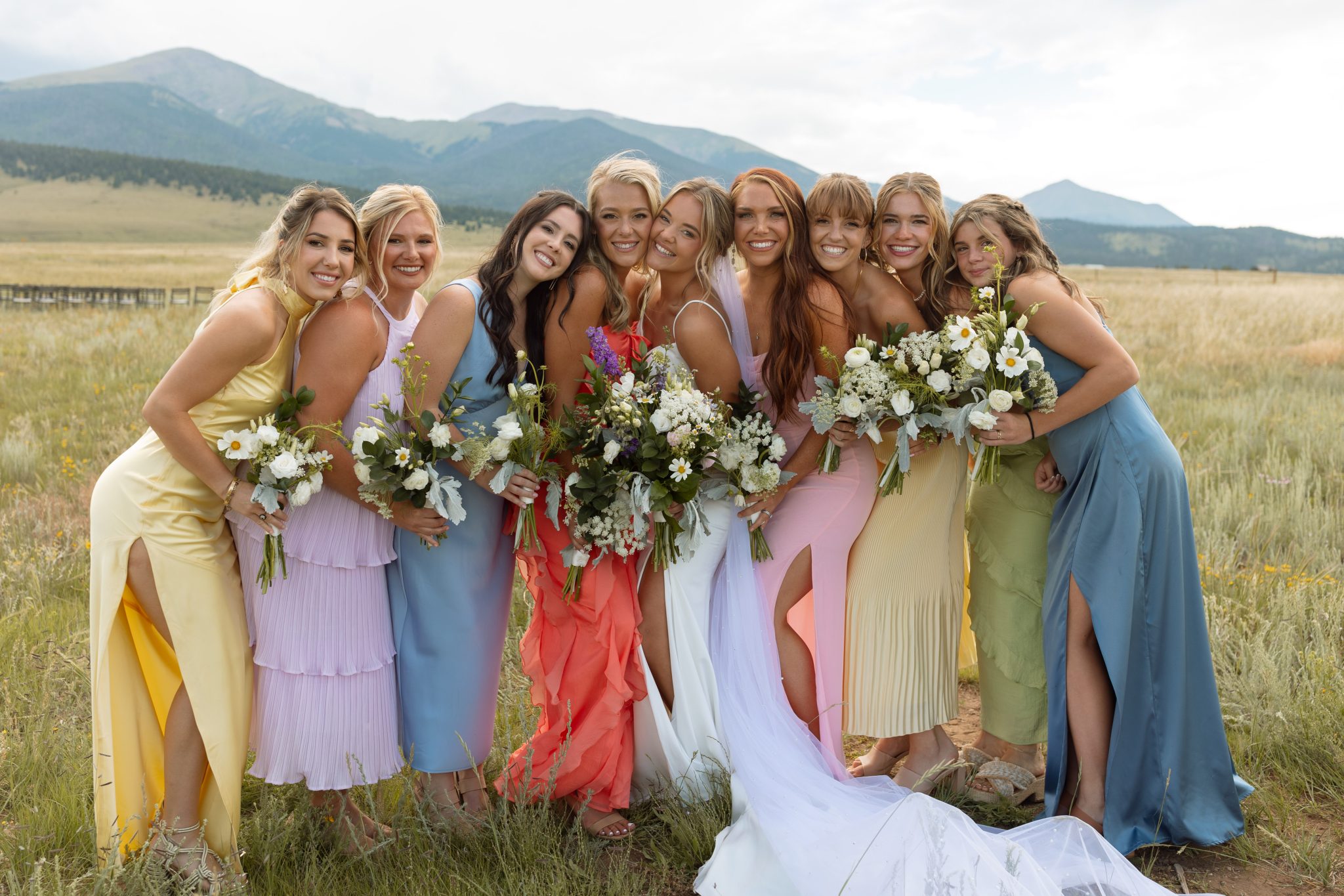 Bride and bridesmaids in colorful dresses smiling together in a mountain meadow at a Three Peaks Ranch wedding with Sophie Catherine Photo rocky mountain bride.