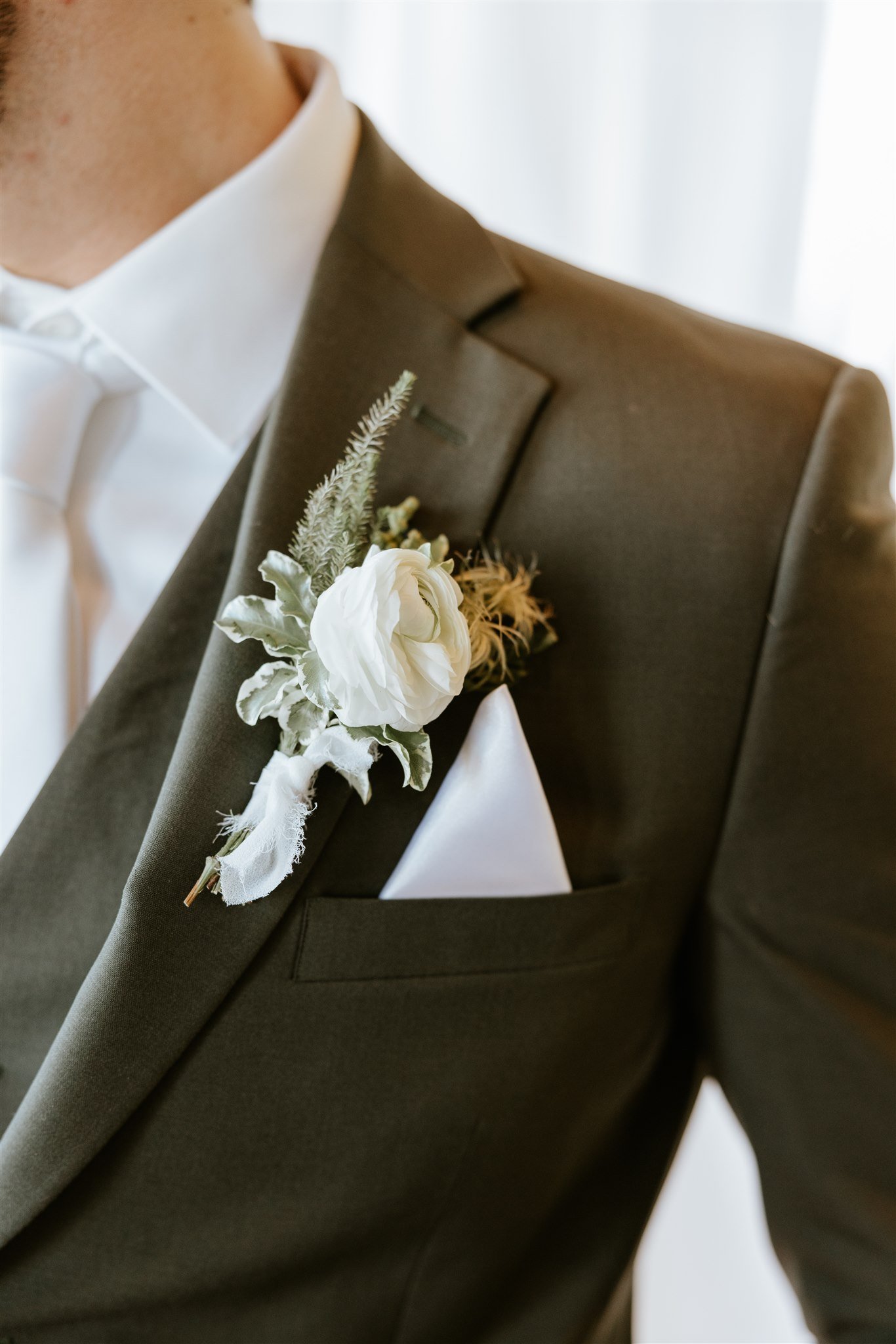 Elegant white ranunculus boutonnière on groom’s olive suit jacket captured at True Wild Distilling styled shoot rocky mountain bride
