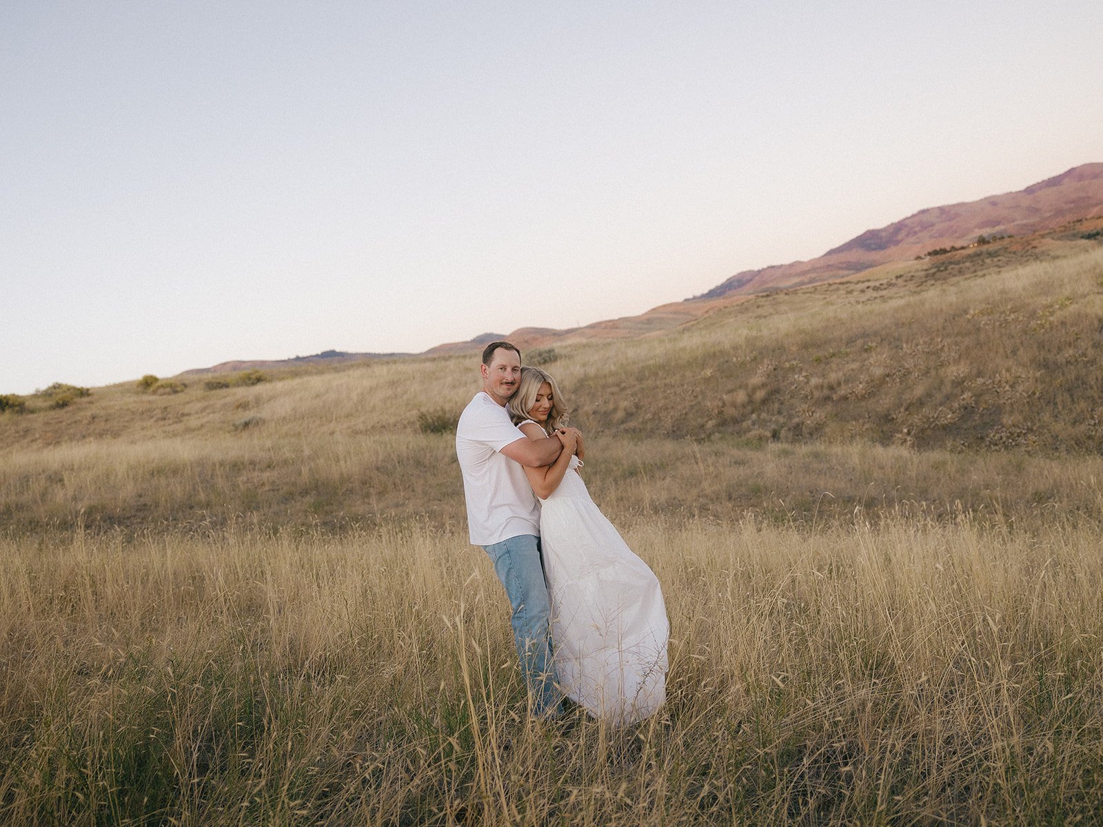 His arms wrapped around her chest in a field of dry grass for a Boise Idaho engagement session with Kayla Lucio Photo rocky mountain bride