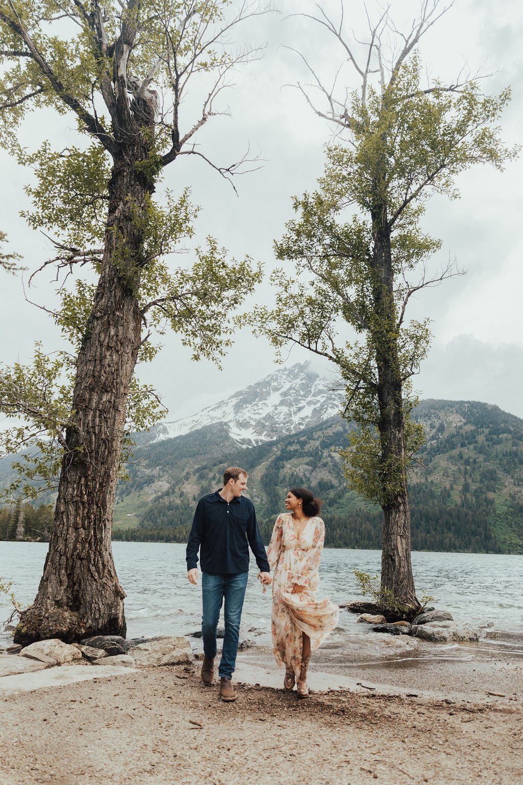 Couple walking hand in hand along the lake with mountain views at Grand Teton National Park engagement session with Ashlyn French Photography rocky mountain bride