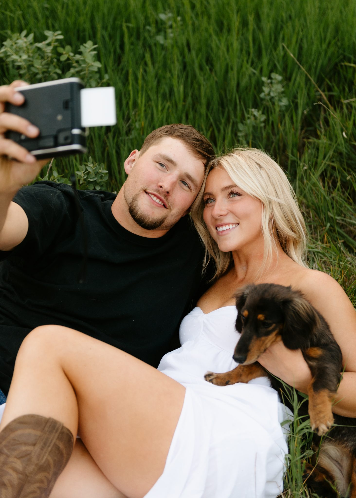 Couple cuddling with their dachshund puppy while taking a selfie during a Scobey Montana engagement session rocky mountain bride.