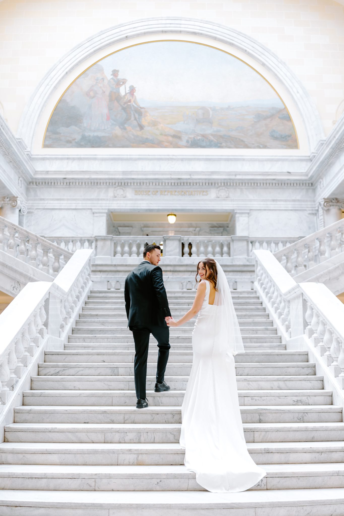 Couple walking up grand marble staircase inside capitol building for Utah wedding bridals rocky mountain bride.