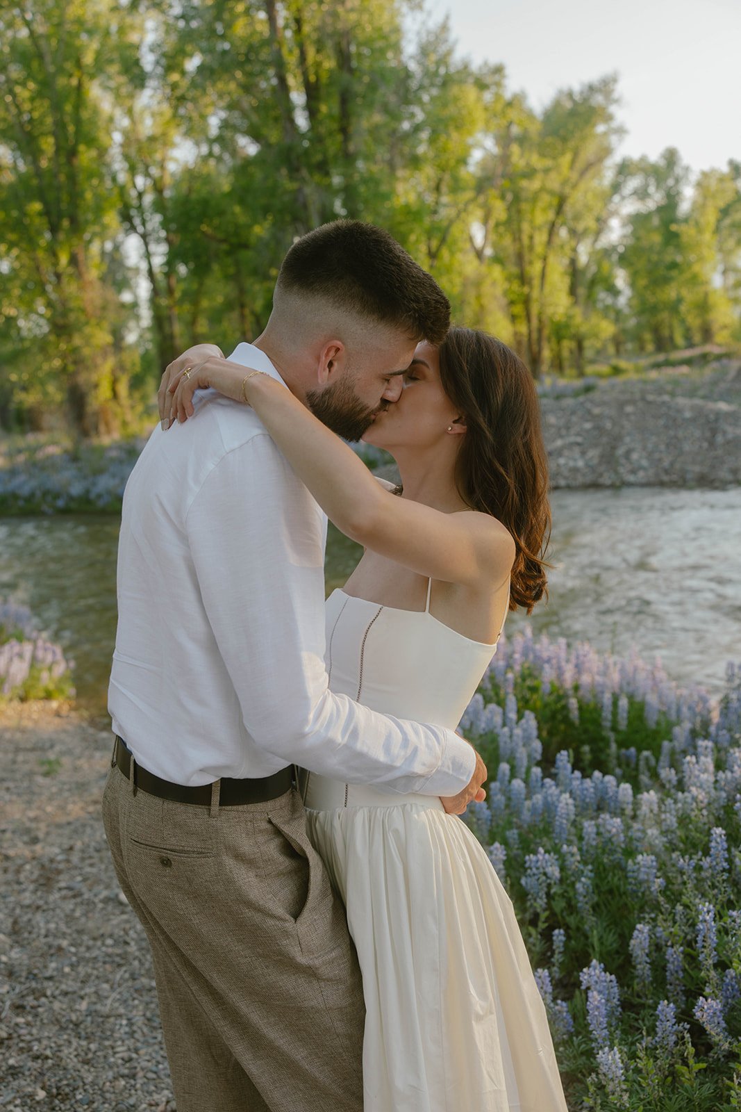 Romantic kiss surrounded by wildflowers and river views during an Evable Photo wyoming engagement rocky mountain bride.