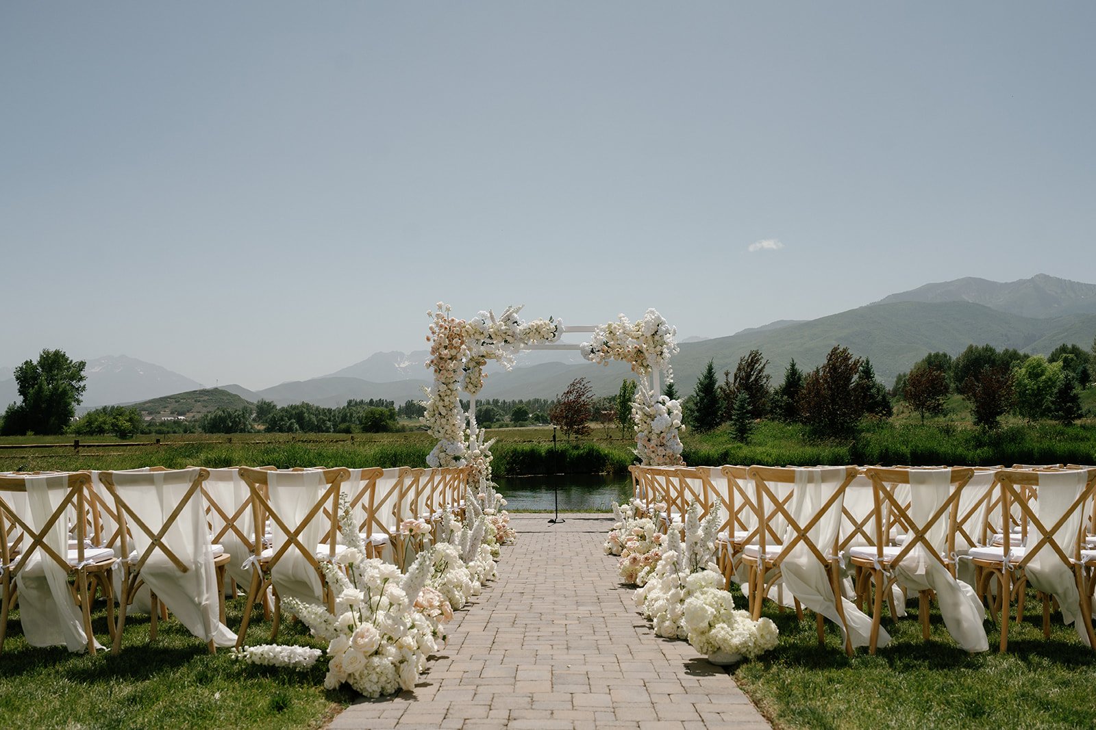 A floral-lined aisle leading to a white arch with soft blooms during a River Bottoms Ranch summer wedding with Shannon Yen Photography rocky mountain bride.