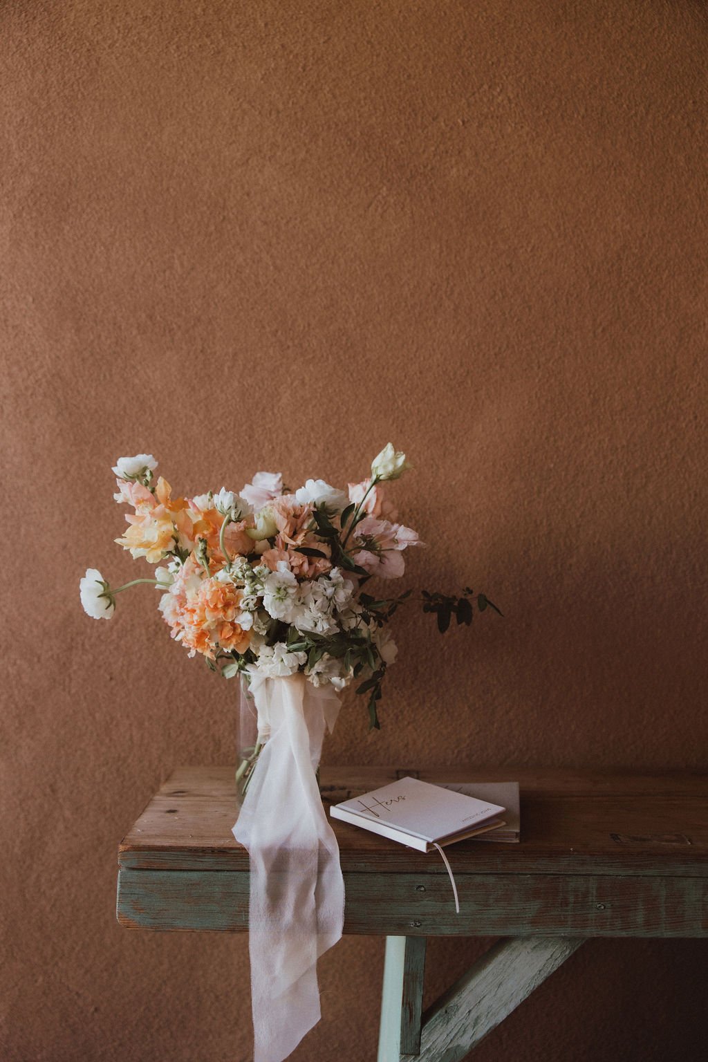 A soft pastel bridal bouquet rests on a rustic turquoise table beside handwritten vow books, capturing the delicate details of a Spring New Mexico private estate wedding Rocky Mountain Bride.