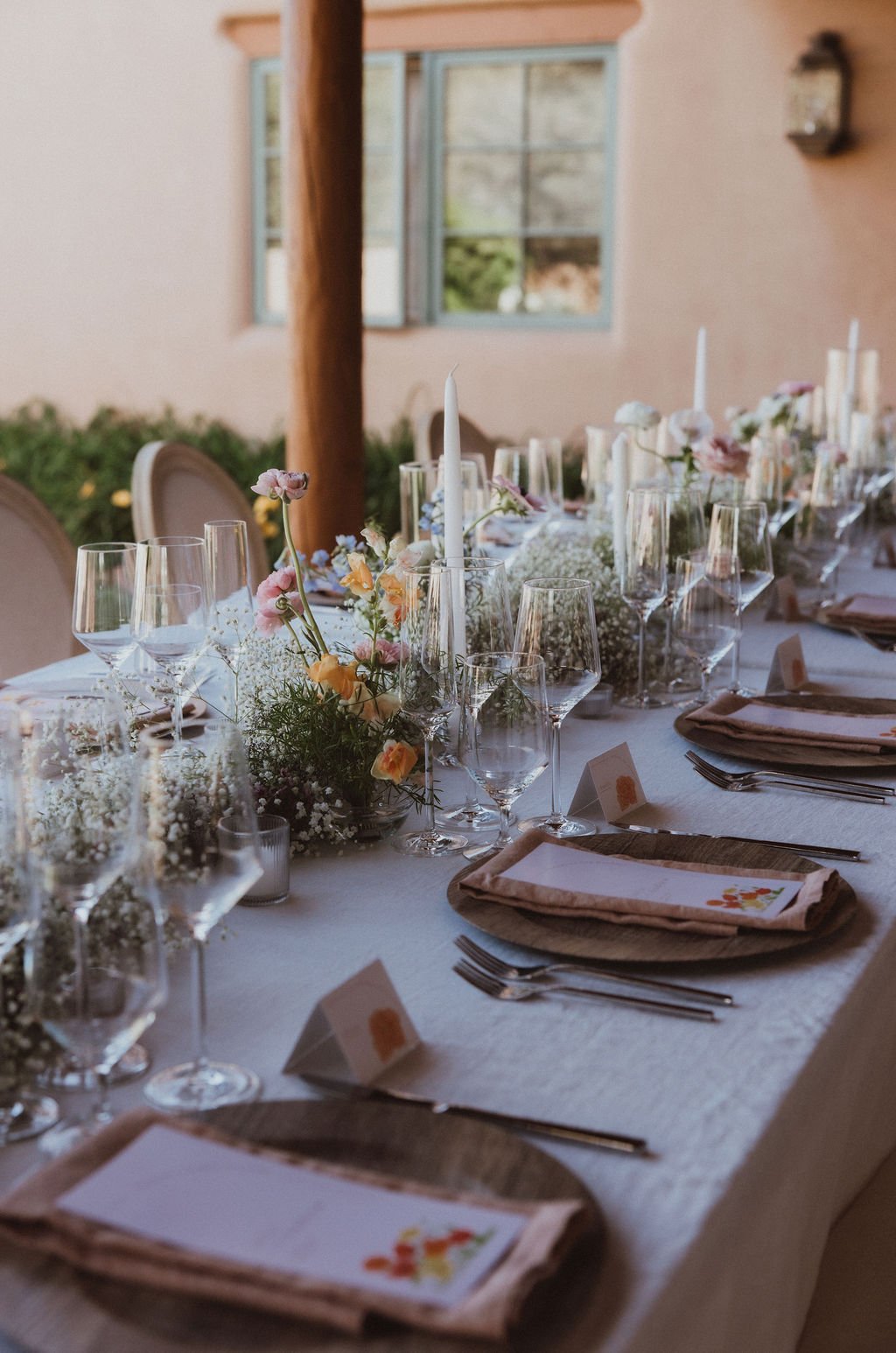 An elegant outdoor tablescape featuring soft blush florals, taper candles, and wood charger plates under the New Mexico sun for a Spring New Mexico private estate wedding Rocky Mountain Bride.
