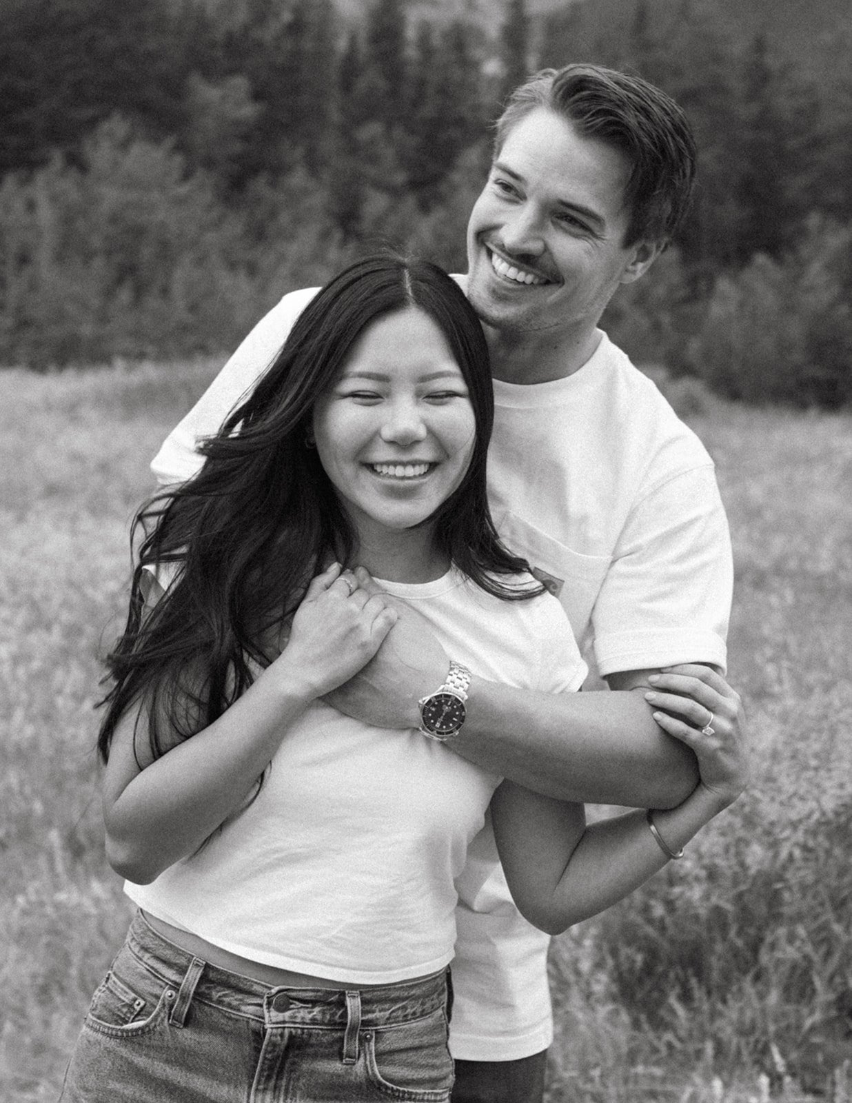 A joyful black-and-white portrait of a smiling couple embracing in a meadow, captured during their canmore mountain quarry lake albert engagement taylor dawning photography session.