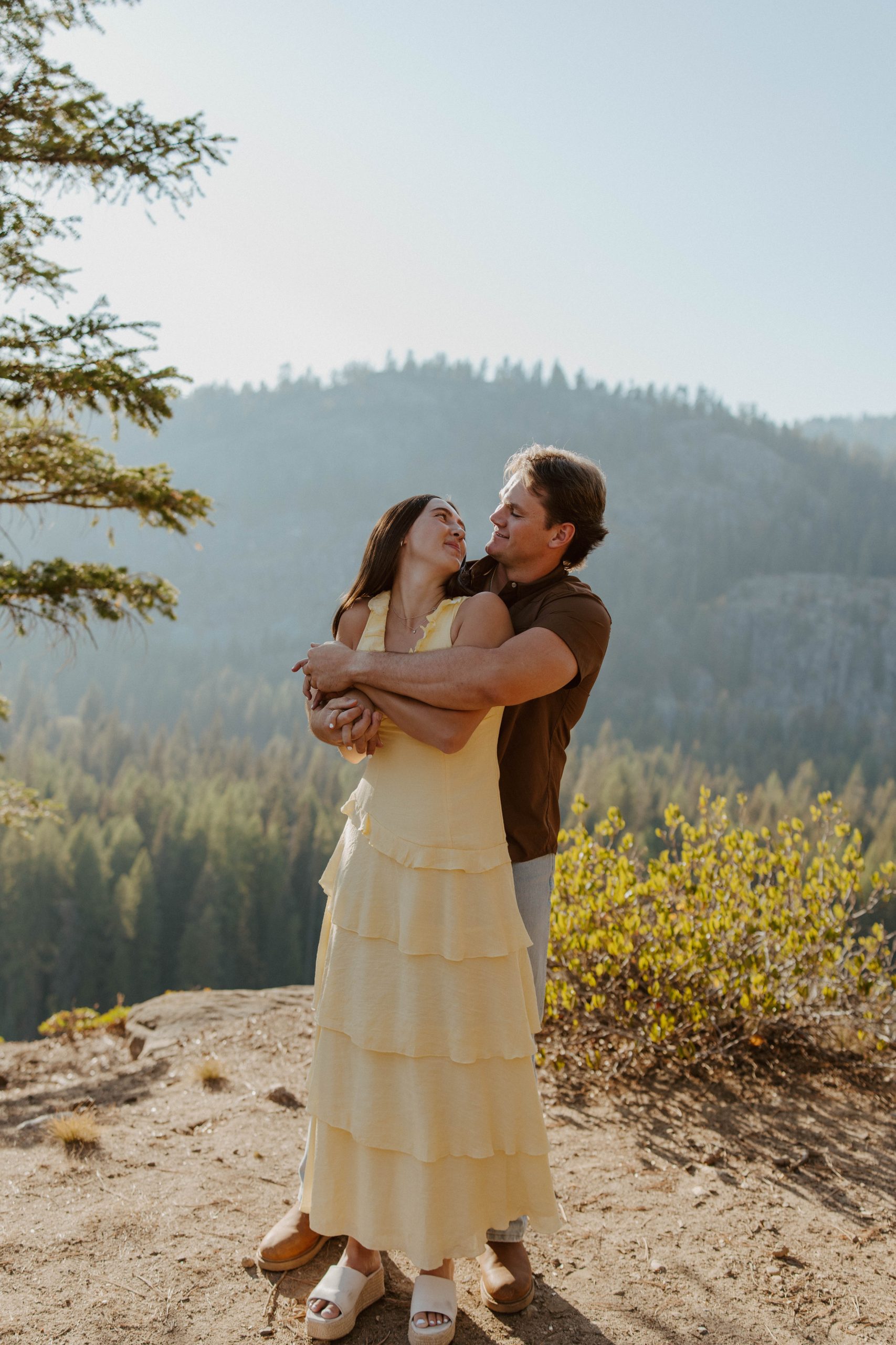 Couple embracing and smiling at each other on a scenic cliffside during a Quinn Briley Photography fall engagement session McCall Idaho rocky mountain bride.