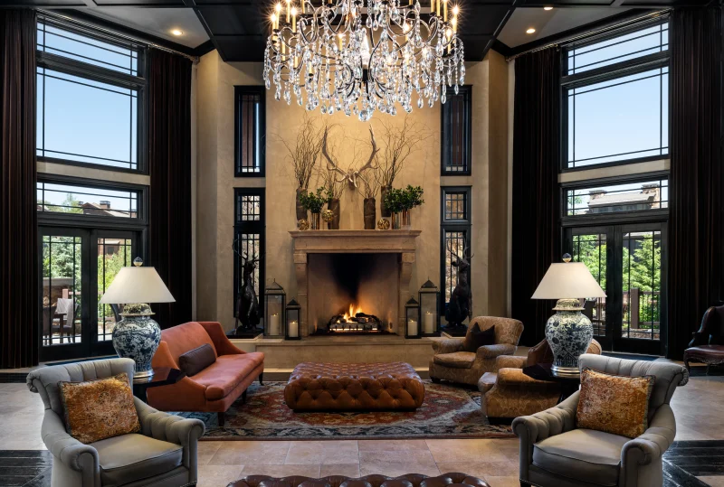 Elegant hotel lobby with a crystal chandelier, fireplace, leather seating, tall windows and warm mountain lodge-inspired decor.